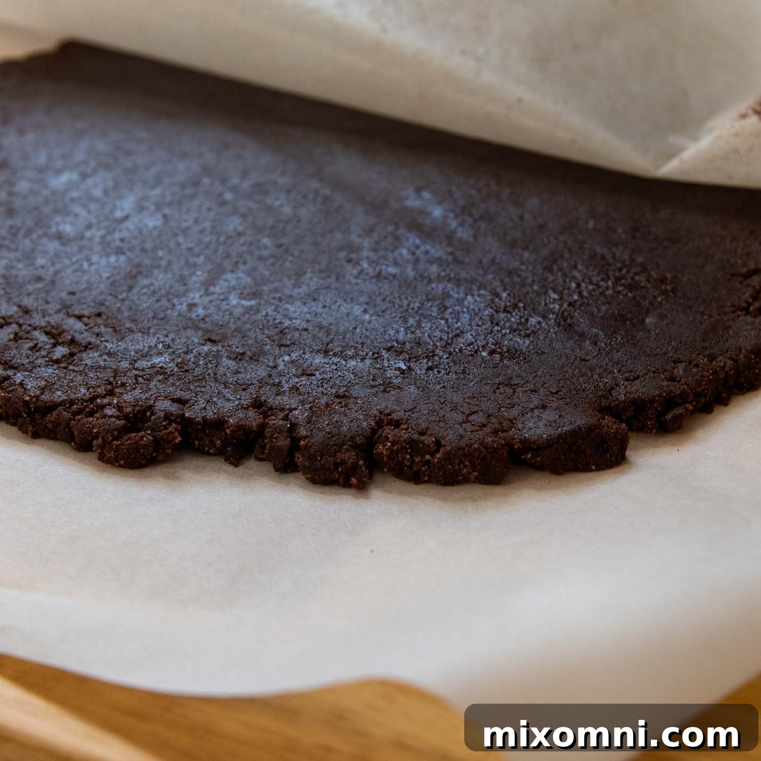 Cookie dough being carefully rolled between two sheets of parchment paper with a rolling pin.