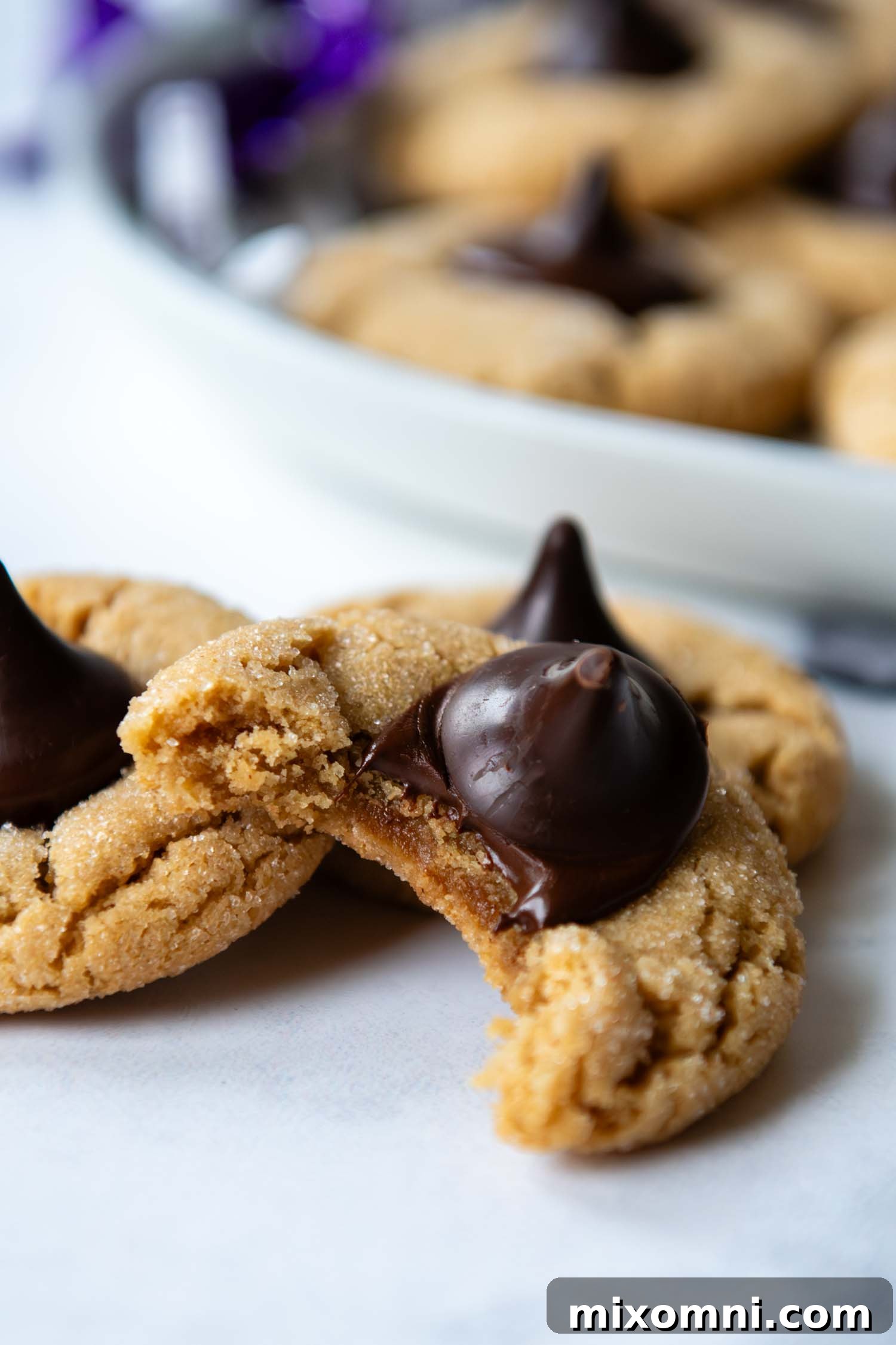 Close up of a freshly baked, soft gluten-free peanut butter blossom cookie with a chocolate kiss pressed into its center, revealing its irresistible texture.