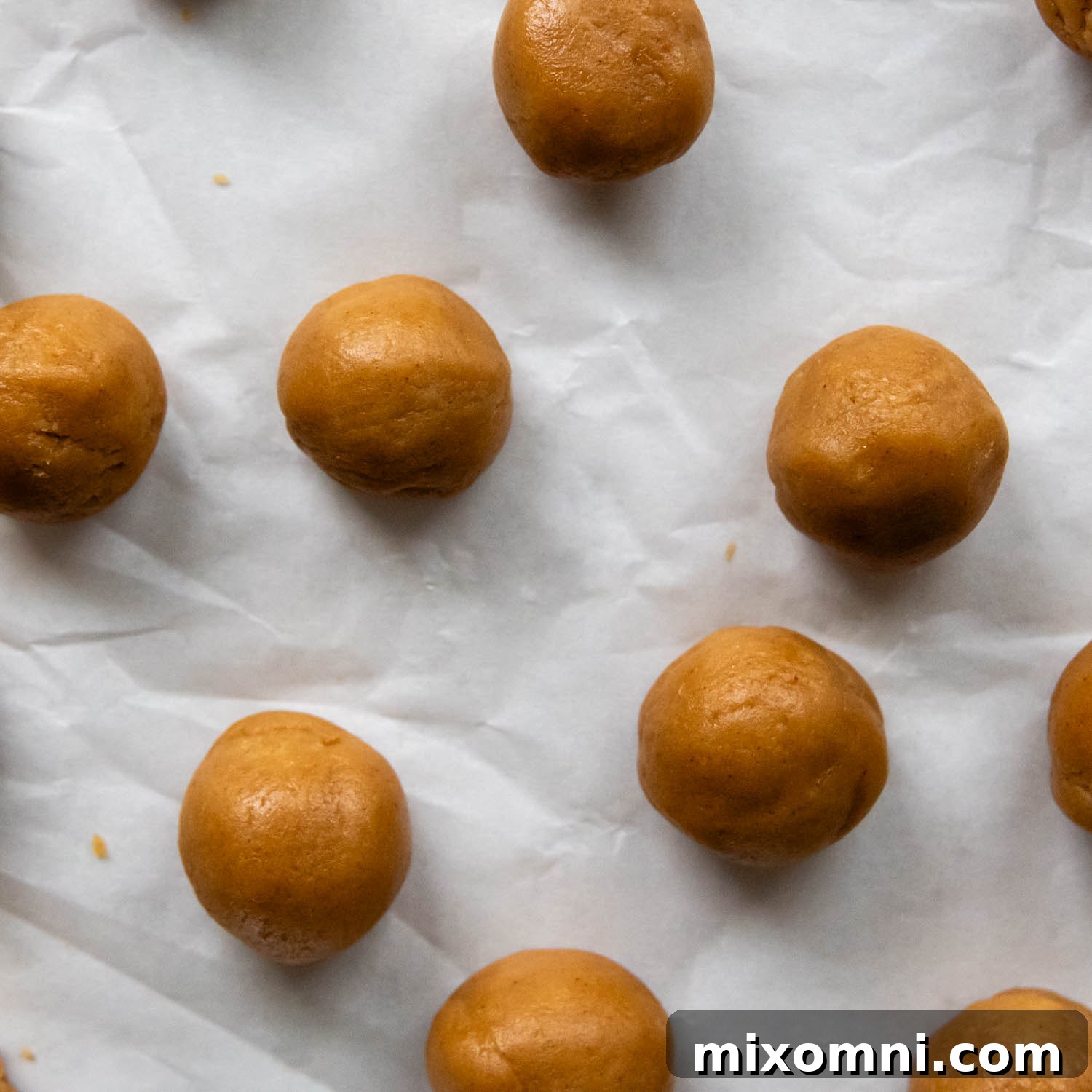Rows of unbaked gluten-free peanut butter cookie balls, evenly spaced on parchment-lined baking sheets.