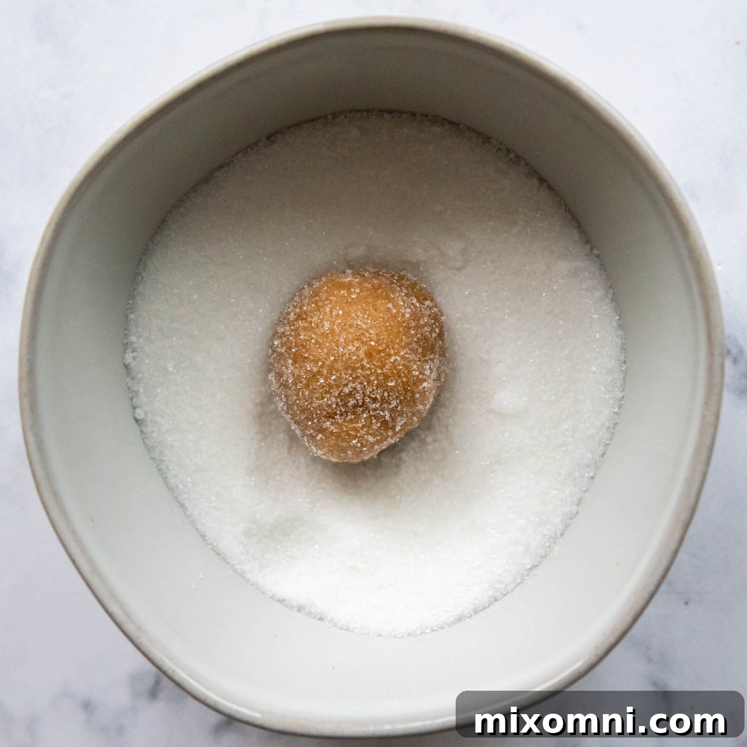 A single gluten-free peanut butter cookie dough ball being rolled in granulated sugar.