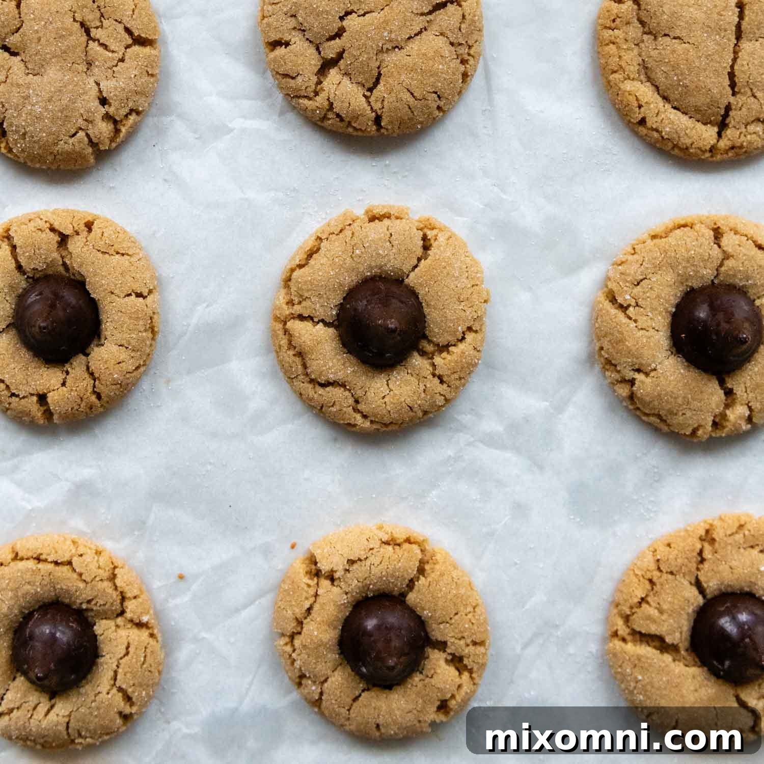 Warm cookies on parchment paper with a chocolate kiss gently pressed into the center of each, ready to cool and set.