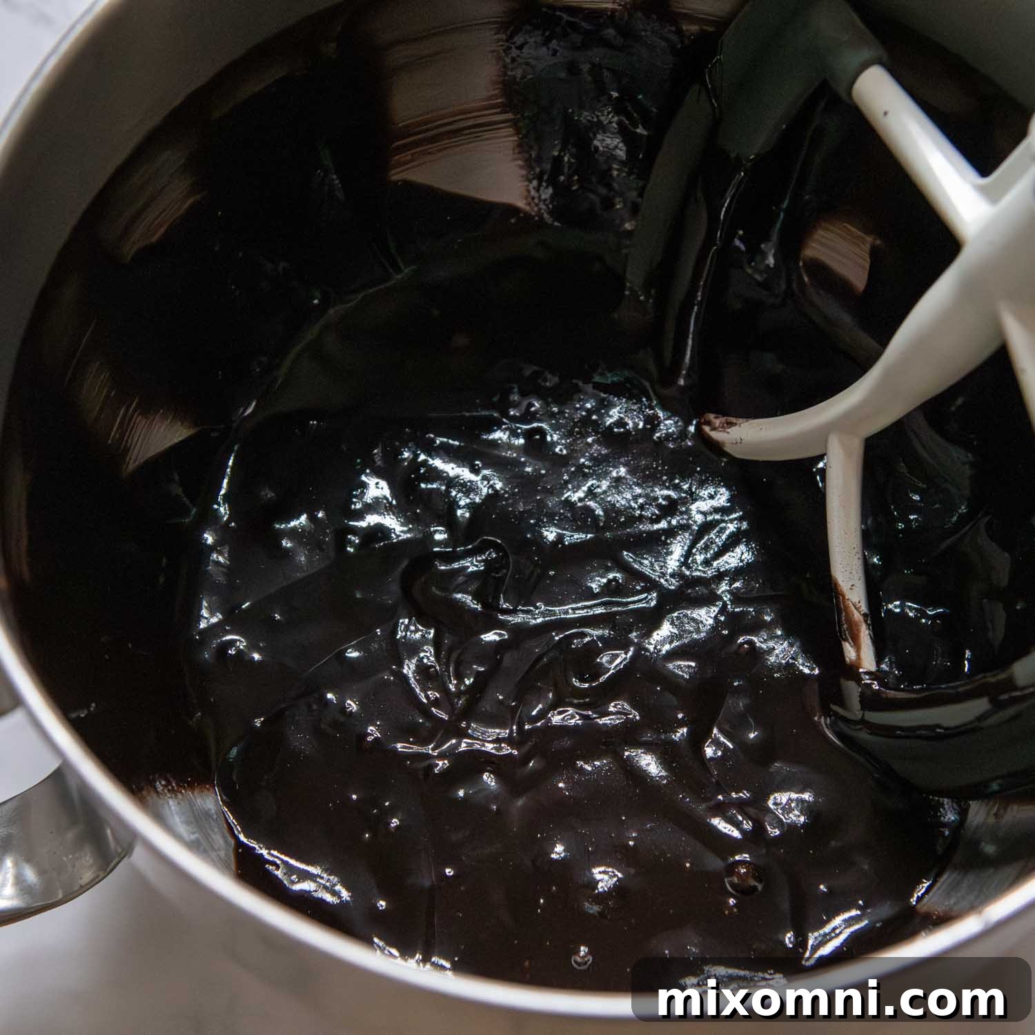 Rich chocolate cake batter being expertly mixed in a stand mixer, showcasing its smooth consistency.