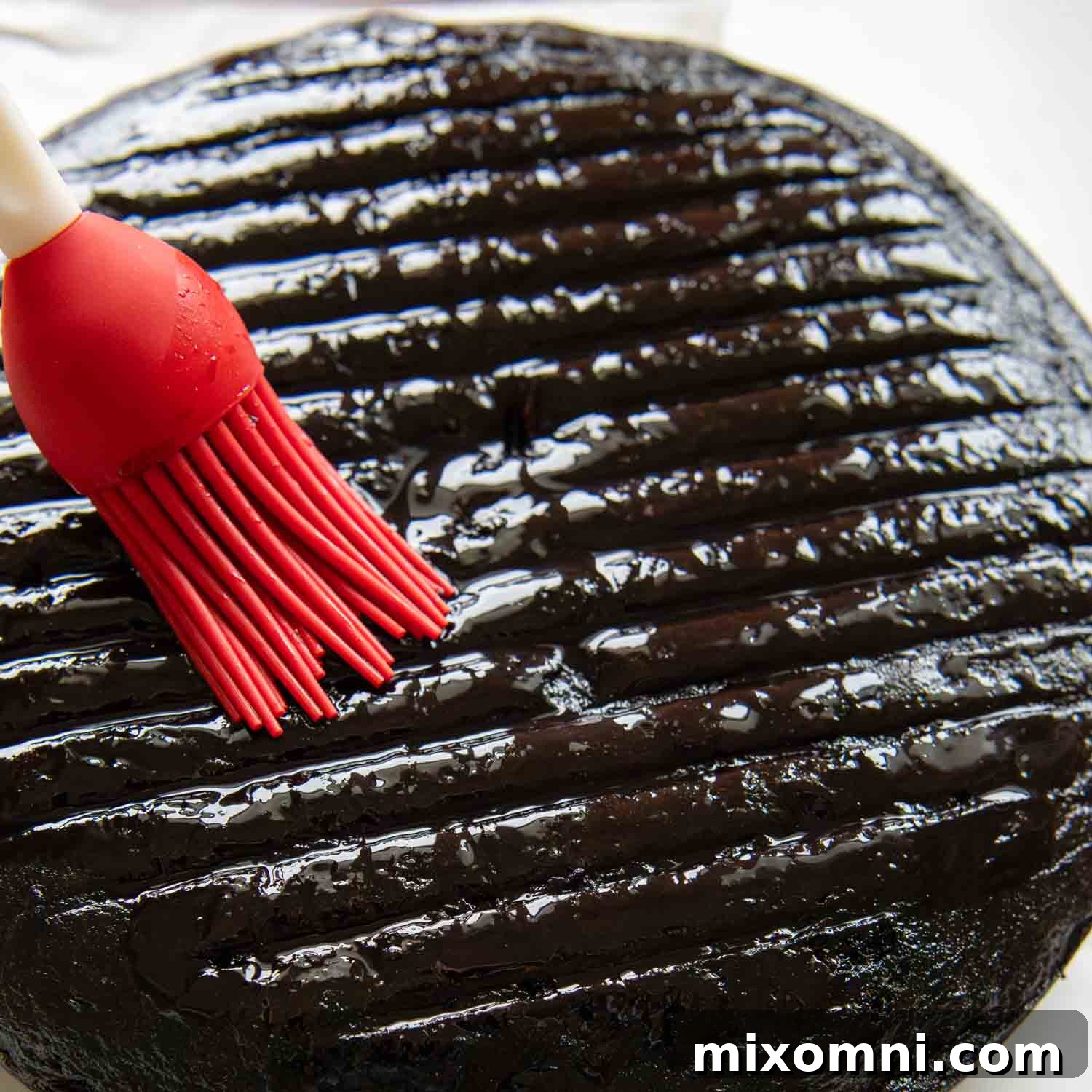 Cherry syrup being carefully brushed onto a moist chocolate cake layer, preparing it for the next step of assembly.