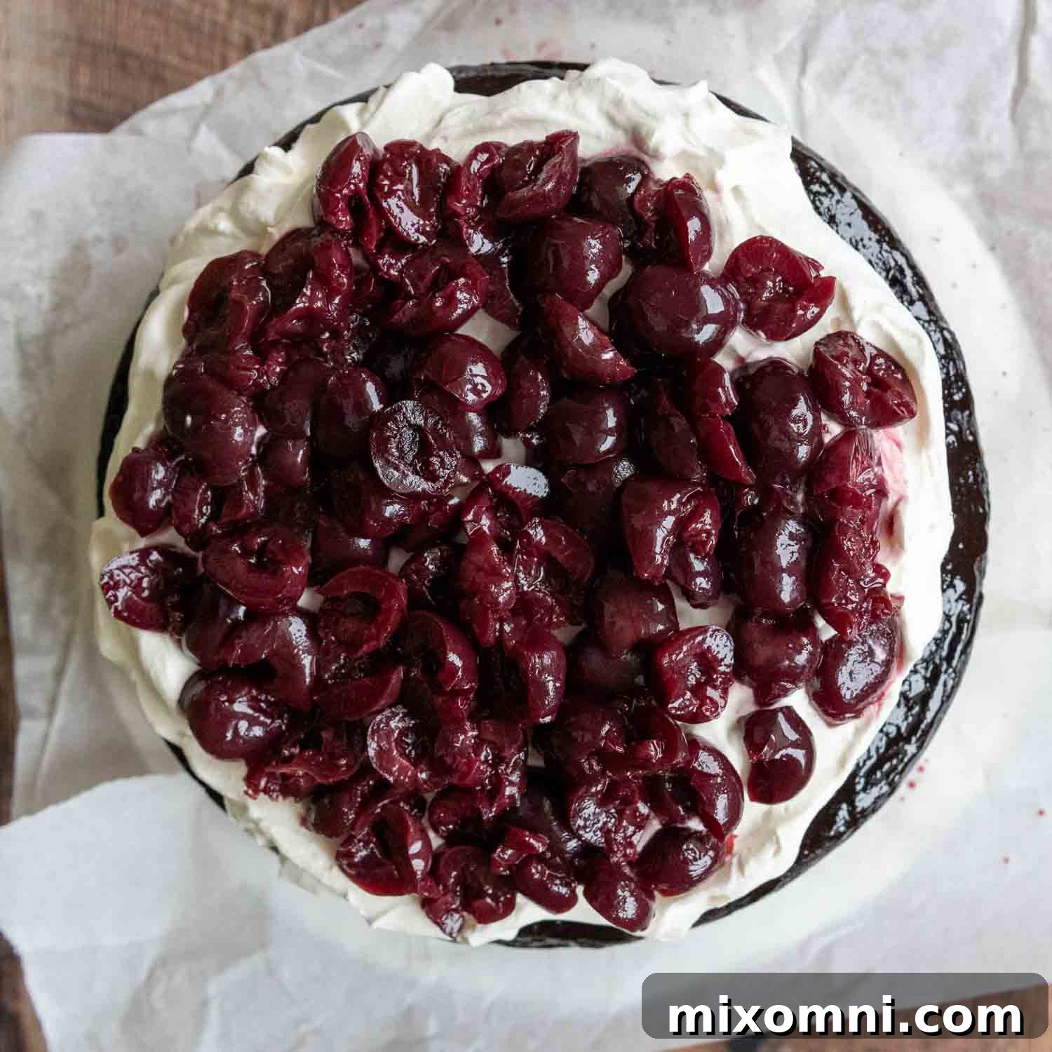 An overhead shot showing plump, halved cherries artfully arranged on a thick layer of whipped cream, ready for the next cake layer.
