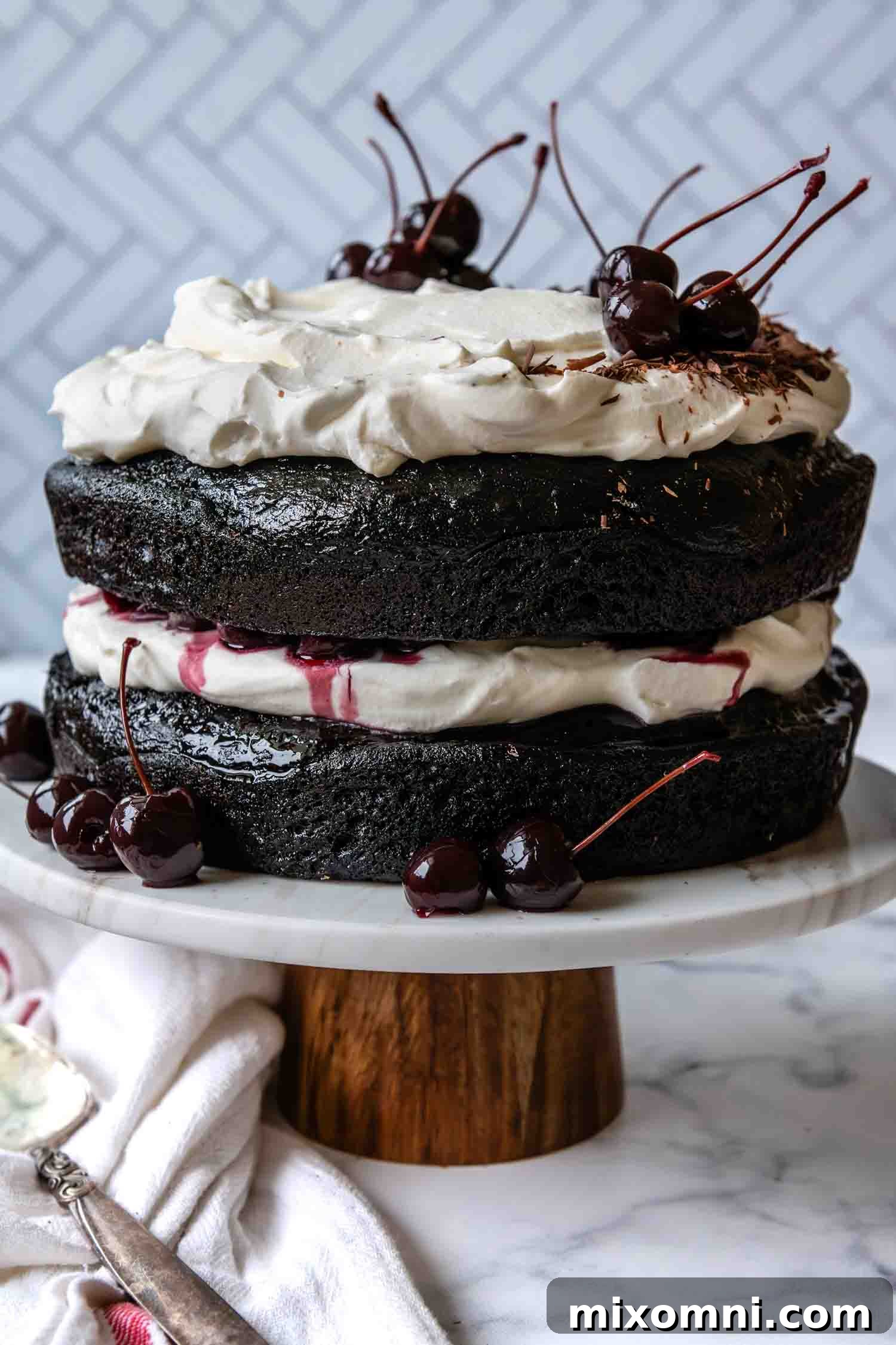 The impressive finished Gluten-Free Black Forest Cake resting elegantly on a cake stand, adorned with cherries and chocolate shavings.