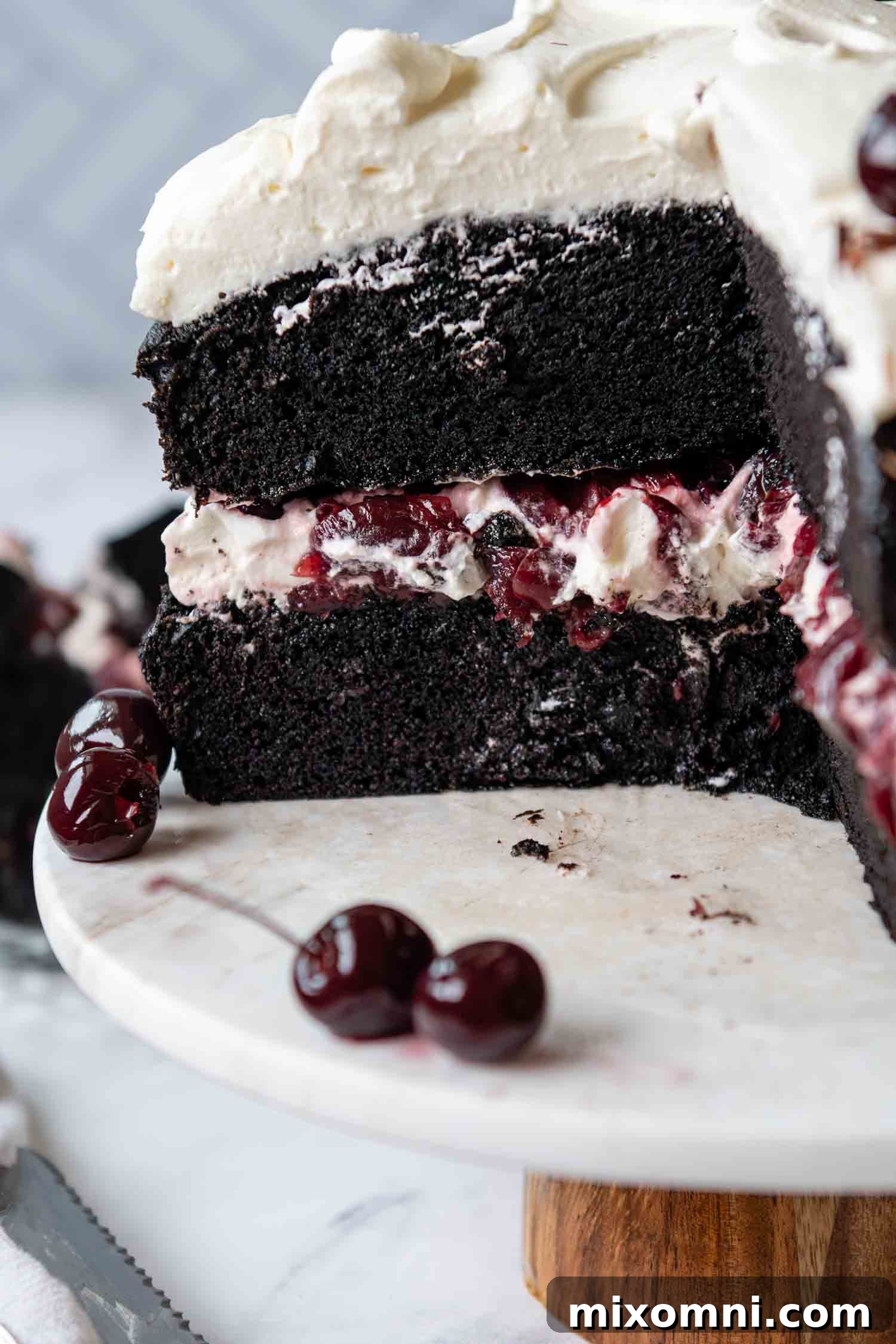 A large, perfectly cut slice of the Gluten-Free Black Forest Cake has been removed, revealing the moist interior layers of chocolate cake, cherry filling, and whipped cream.