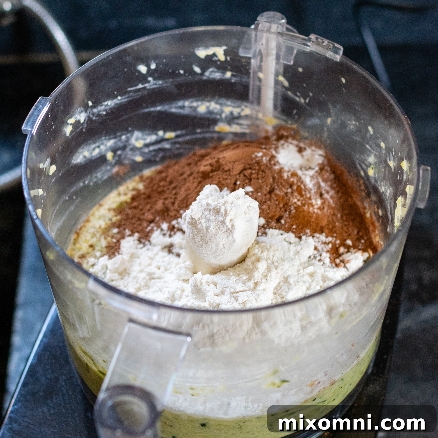 Dry baking ingredients including flour, sugar, and cocoa powder inside a food processor bowl.