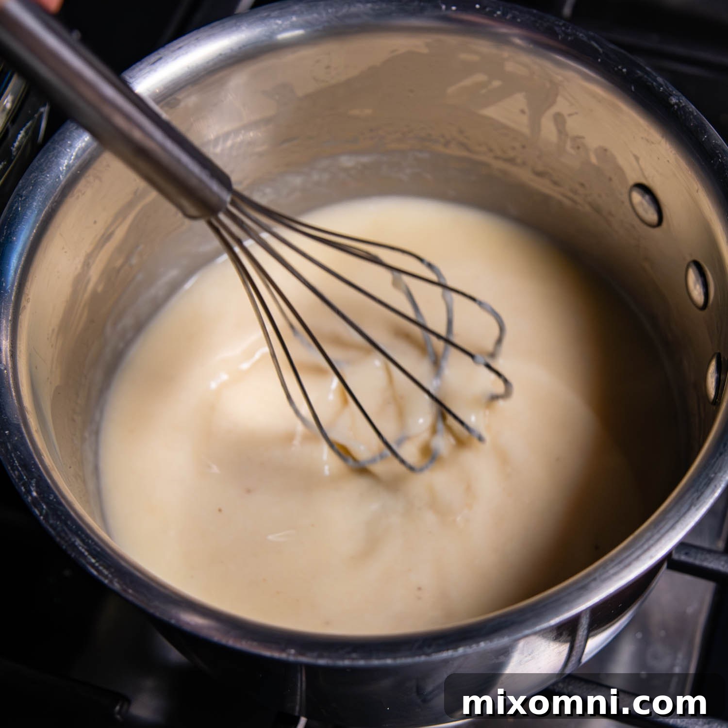 A whisk sitting in a pot of fondue ingredients.