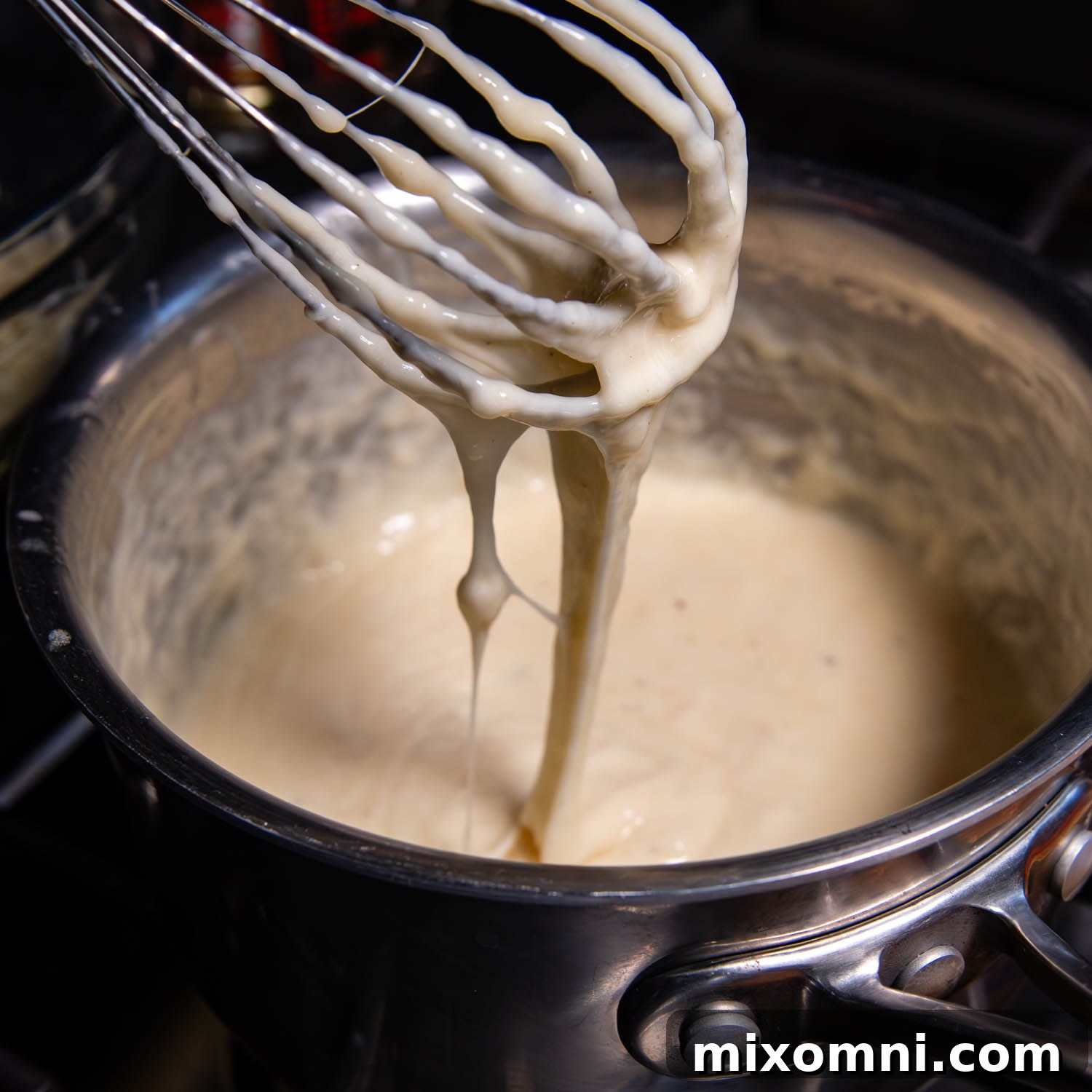 Cheese dripping from a whisk into a pot.