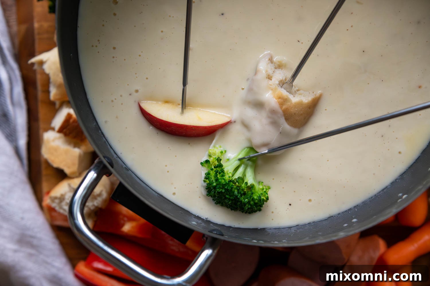 Slice of apple, piece of broccoli and a piece of bread being dipping into a pot of cheese fondue.