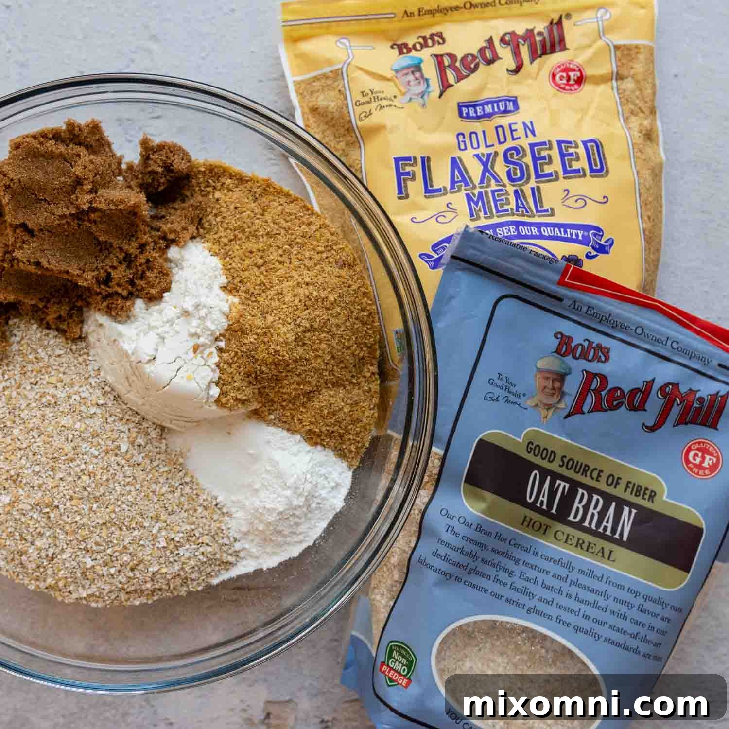 Dry muffin ingredients and packages, including oat bran, gluten-free flour, brown sugar, baking powder, baking soda, salt, and ground flaxseed, arranged neatly on a counter.
