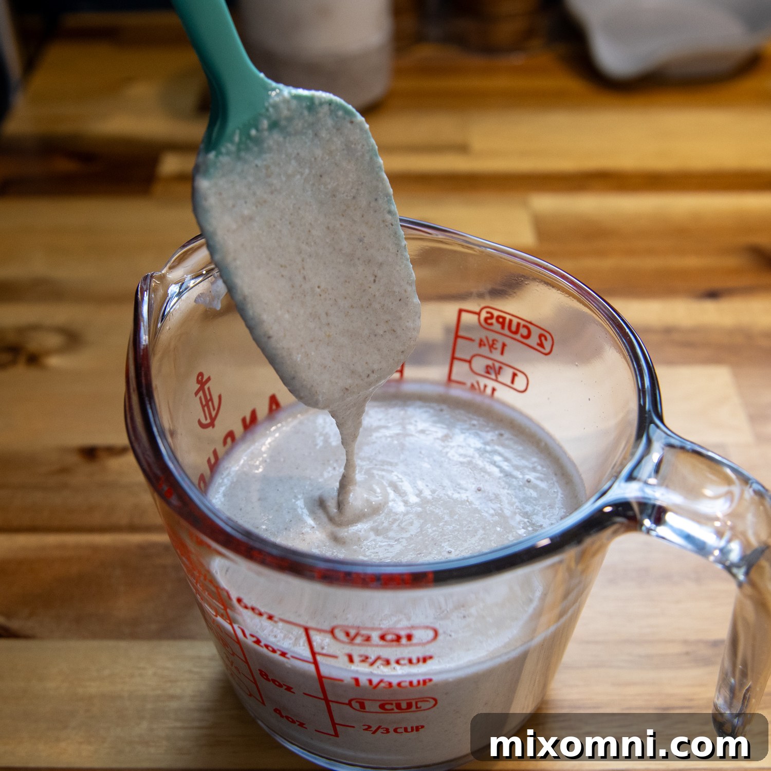 Smooth, thin tortilla batter poured into a glass measuring cup, with a spatula demonstrating its ideal consistency.