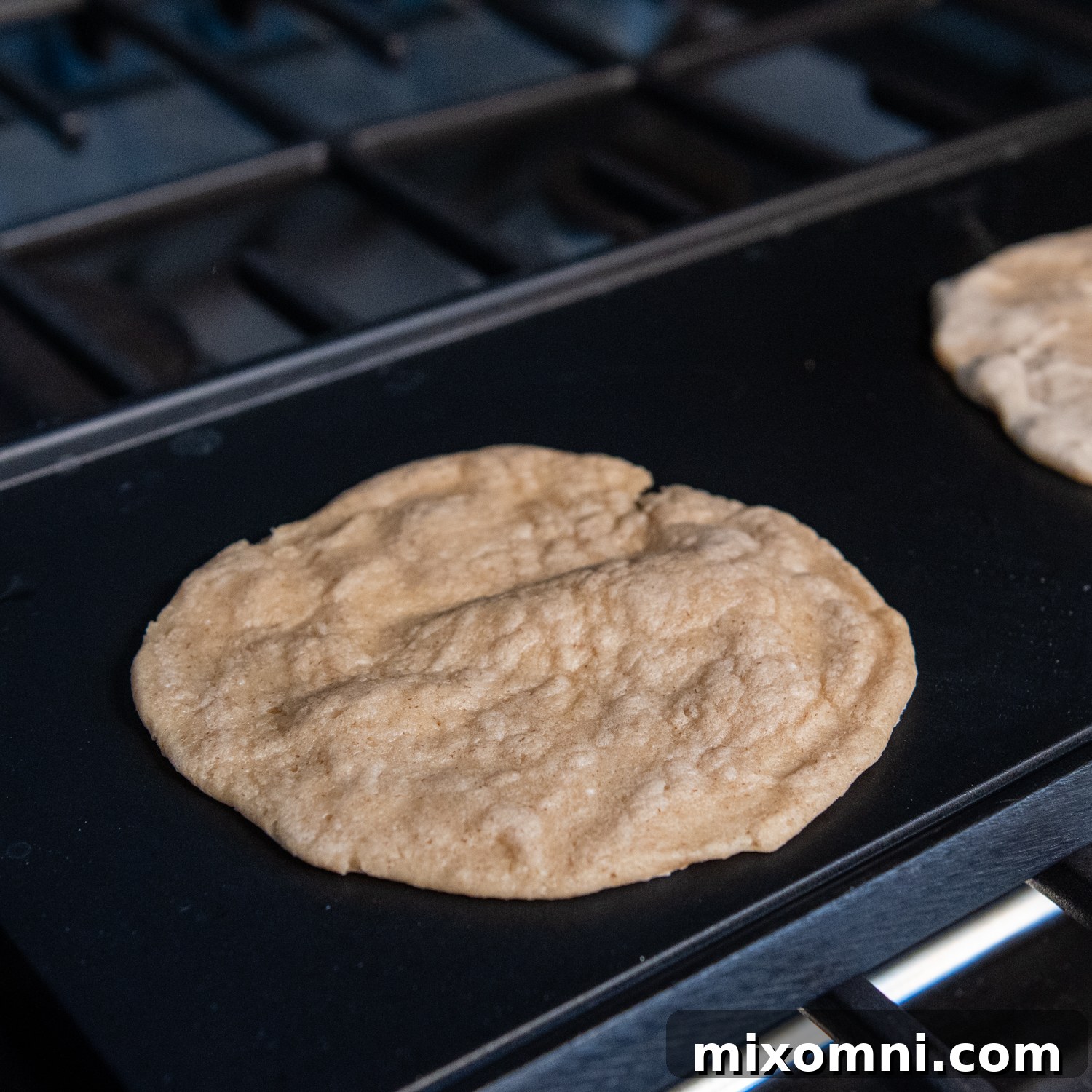 A finished oat tortilla gently puffing up on the griddle, indicating ideal doneness and pliability.