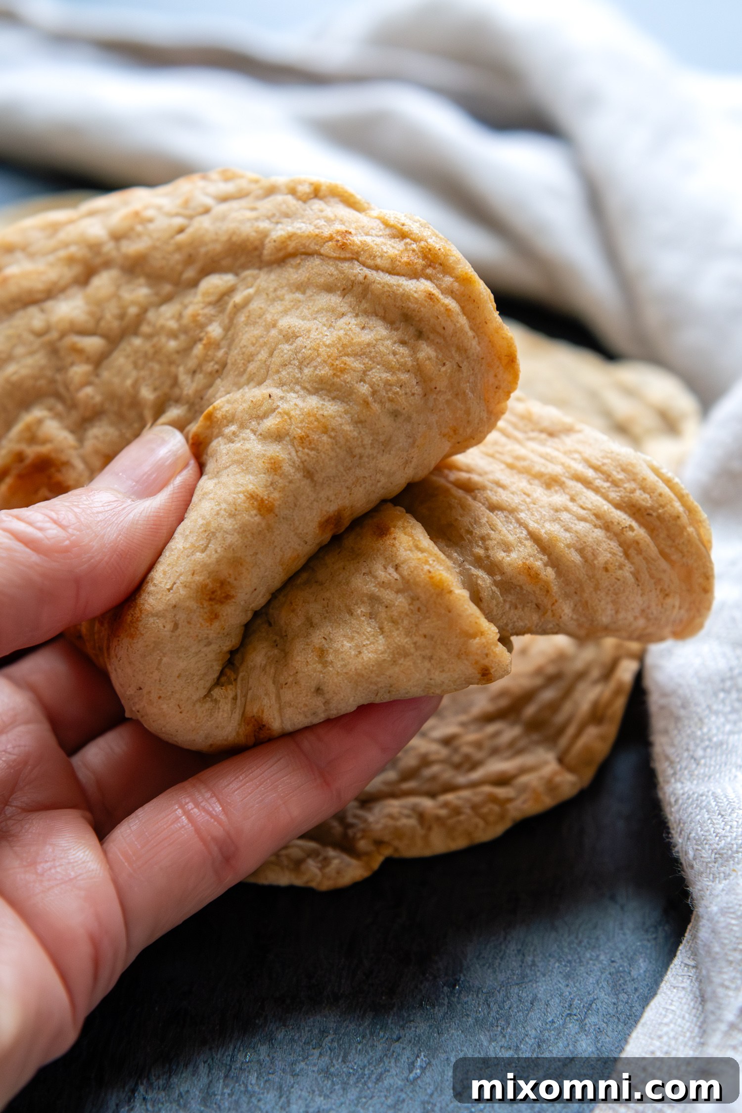 A hand gently holding a perfectly folded gluten-free oat tortilla, showcasing its incredible flexibility.