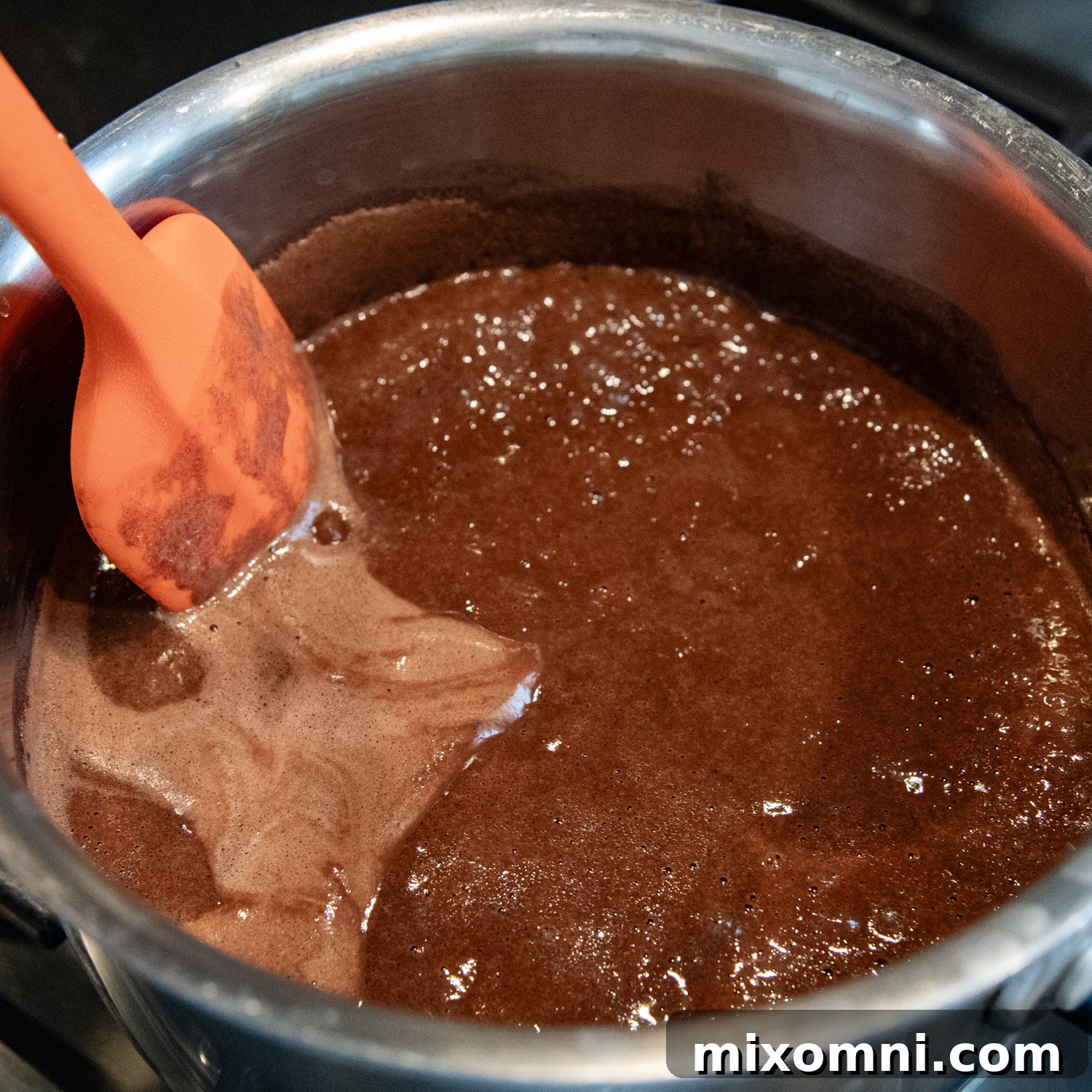 Cake ingredients mixing in a stainless steel bowl with a spatula, demonstrating the hot liquid method.