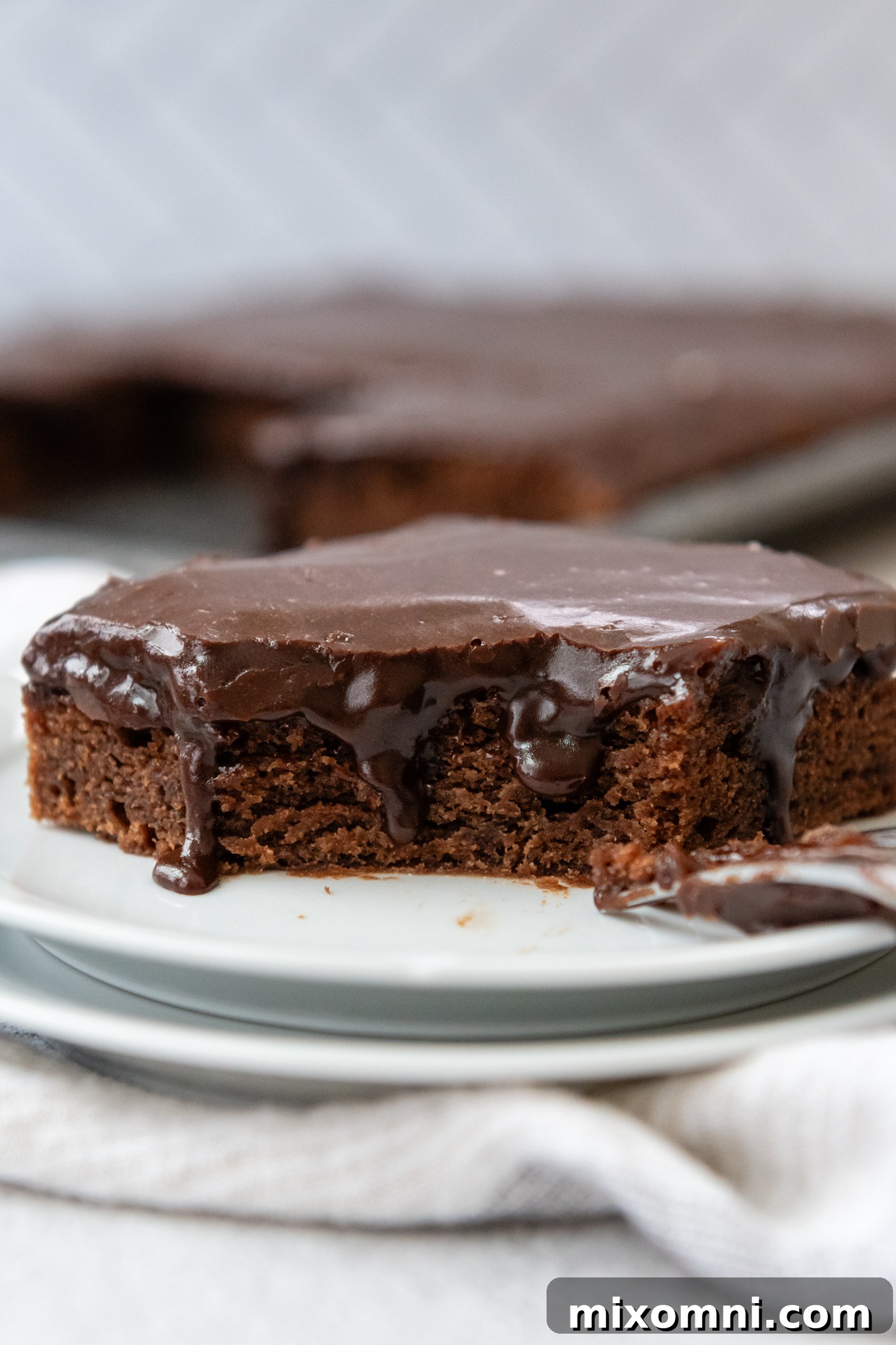 A perfect slice of Gluten-Free Texas Sheet Cake on a white plate, glistening with rich, gooey glaze.