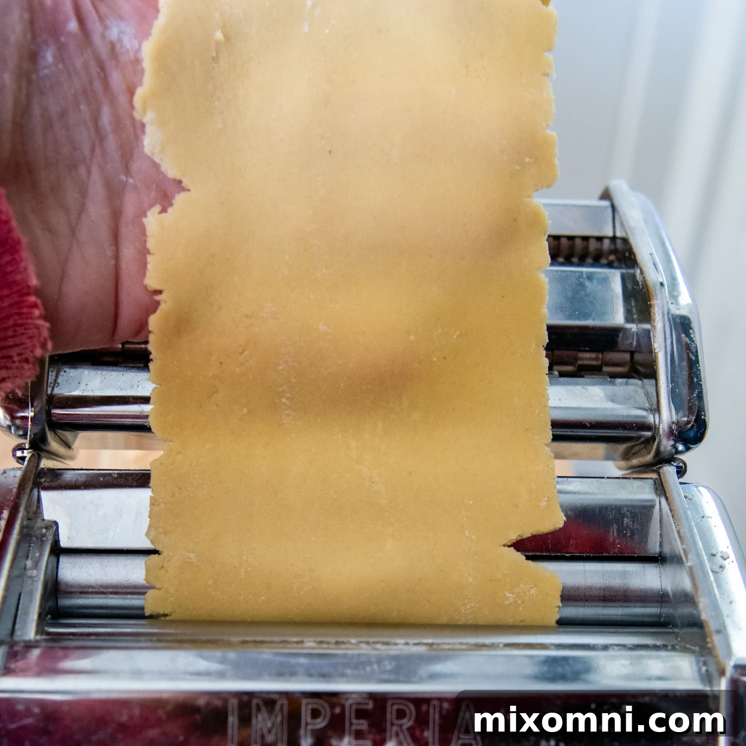 Gluten-free pasta dough being progressively flattened and thinned by a pasta making machine.