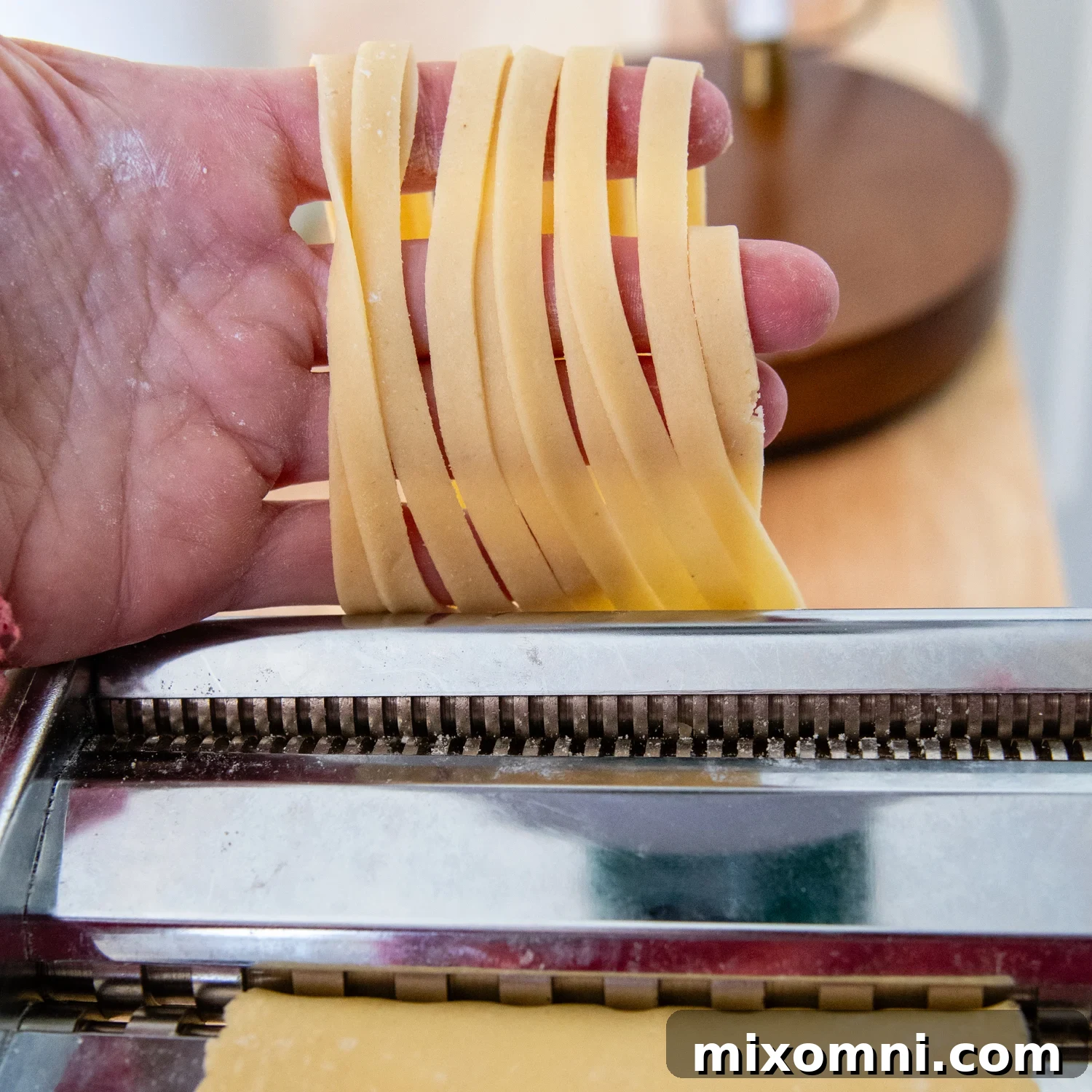 Freshly cut gluten-free fettuccine noodles emerging from a pasta maker, ready to be formed into nests.