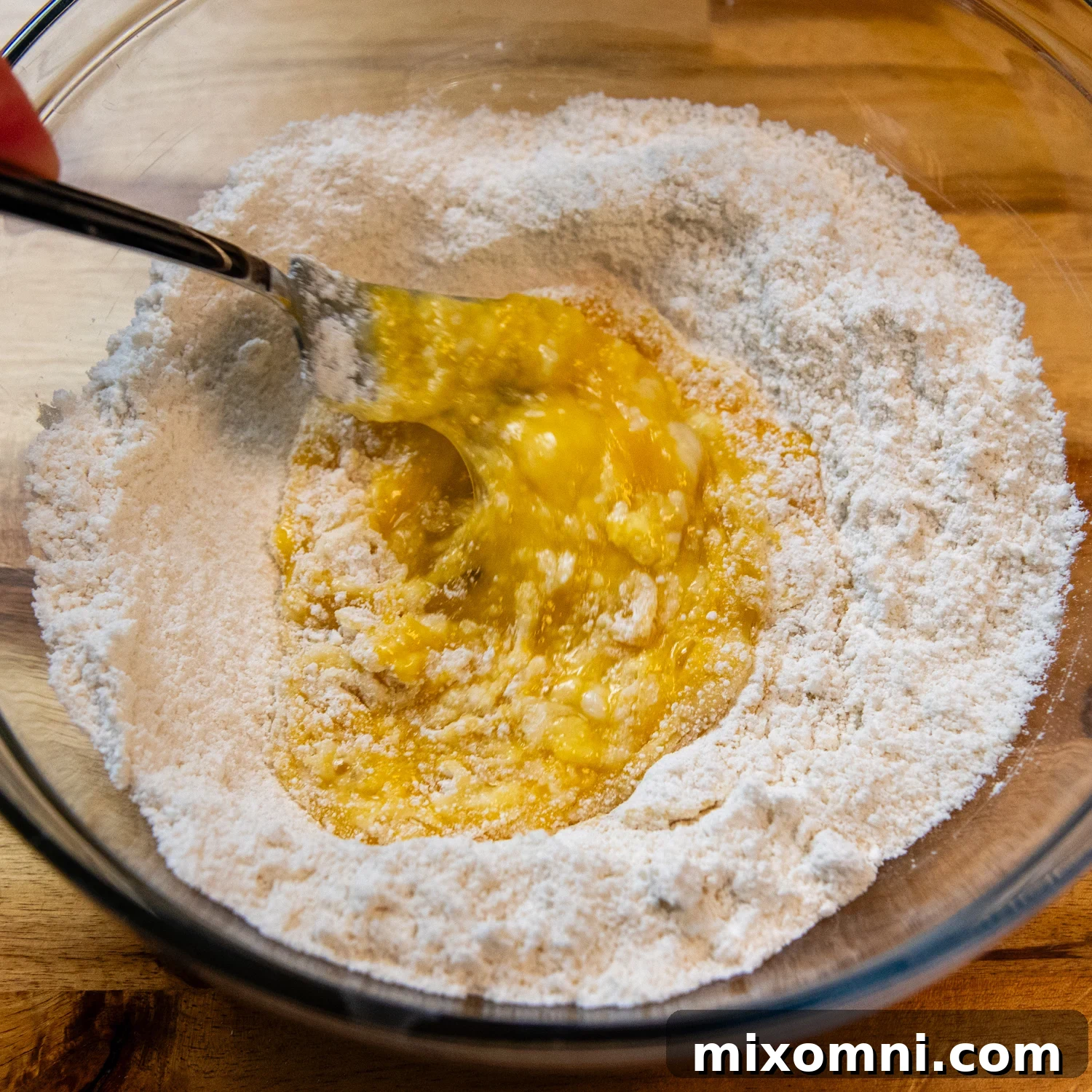 Eggs being added to a well created in a mound of gluten-free flour on a clean surface.