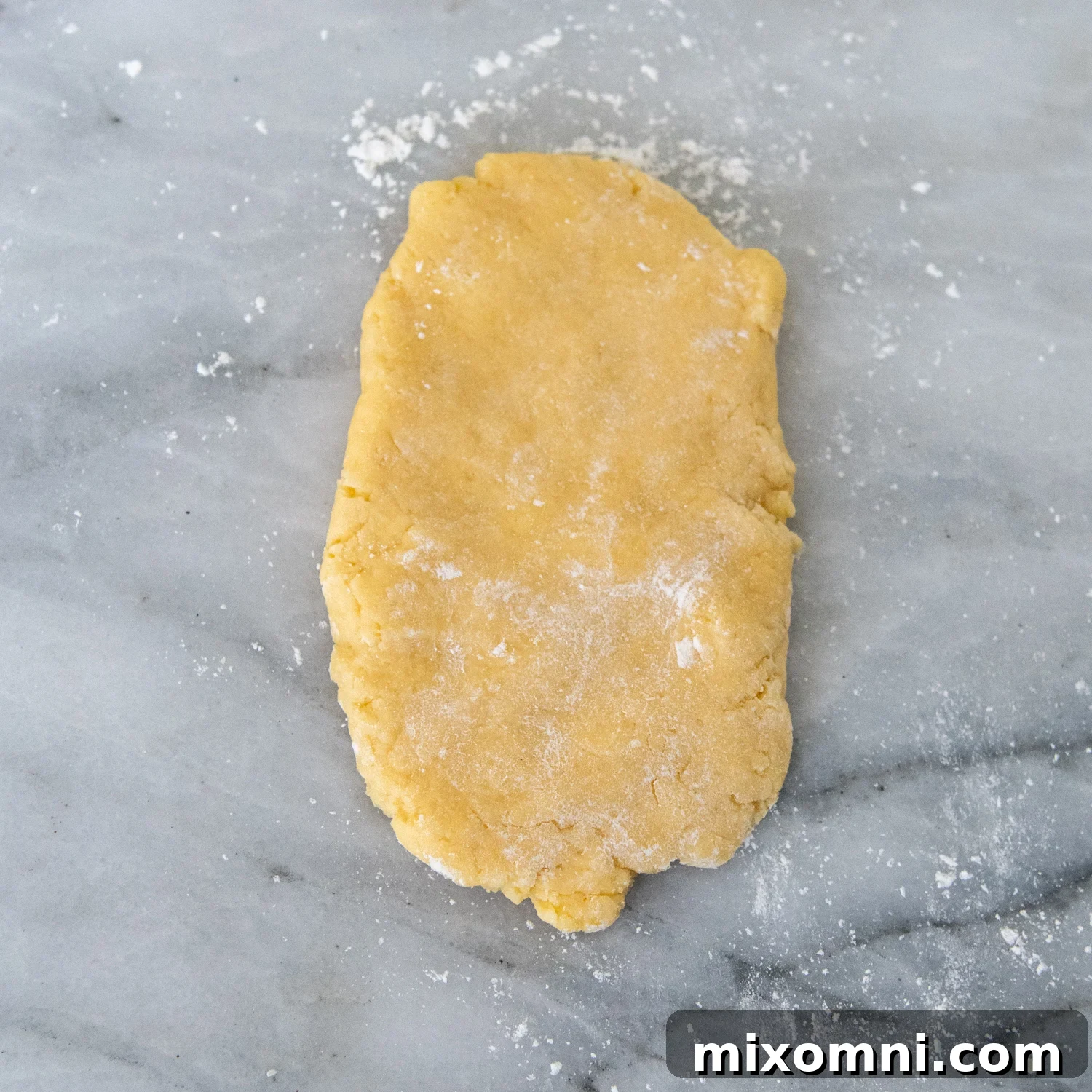 Flattened gluten-free pasta dough sprinkled with flour on a marble surface, ready for the pasta machine.