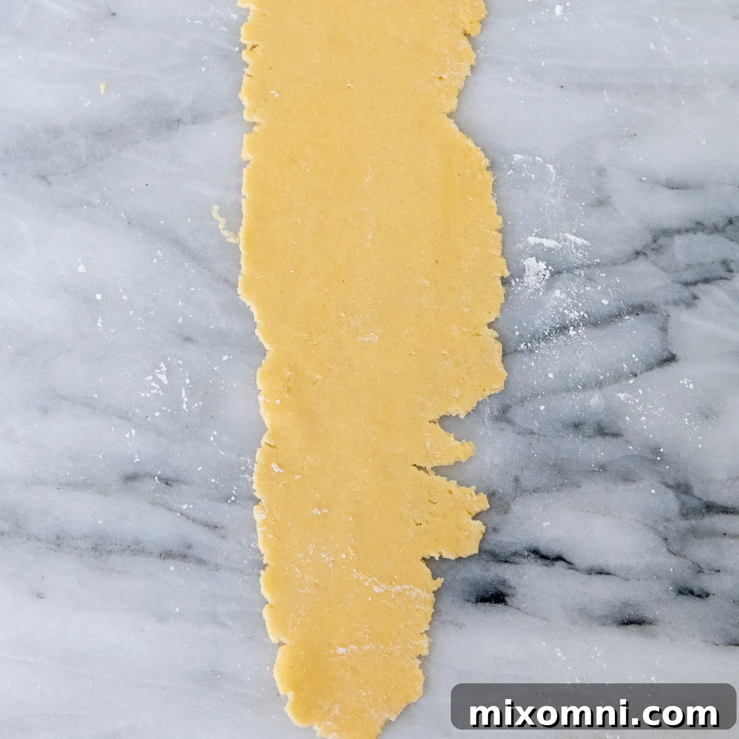 A flattened sheet of gluten-free dough with slightly ragged edges, after its first pass through the widest setting of a pasta machine.