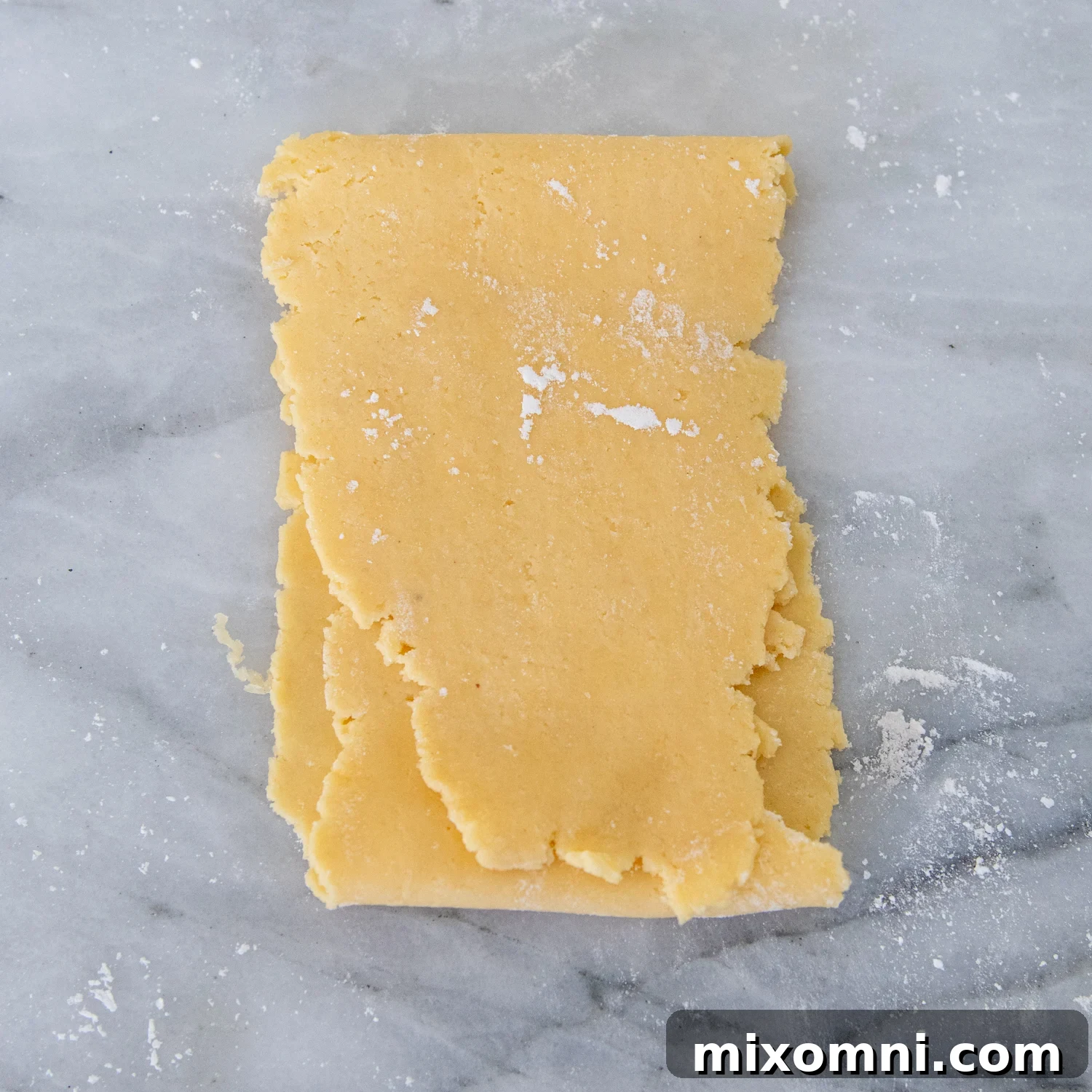 Flattened gluten-free pasta dough folded into thirds, resembling a letter, to prepare for further rolling.