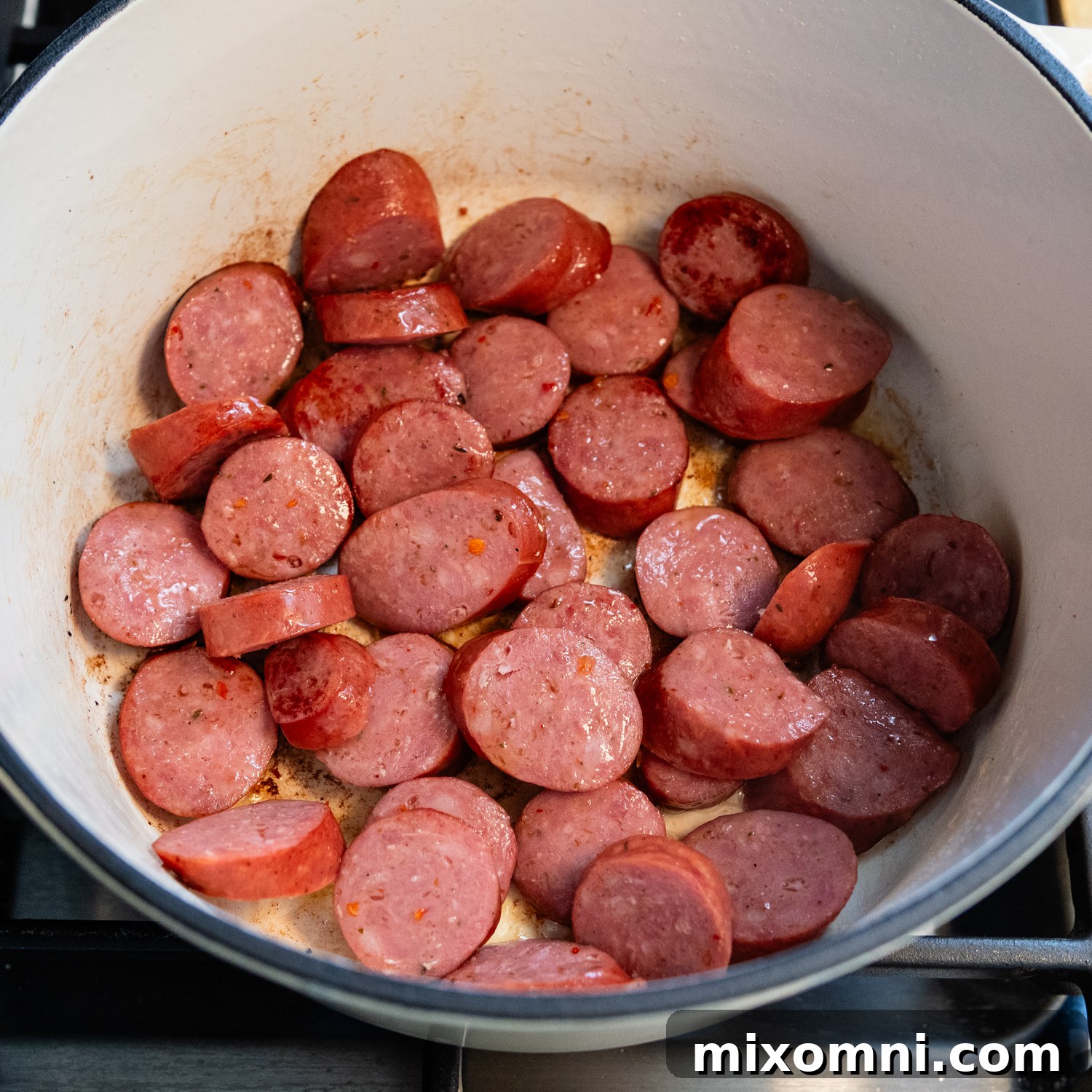 Sliced andouille sausage browning in a large Dutch oven.
