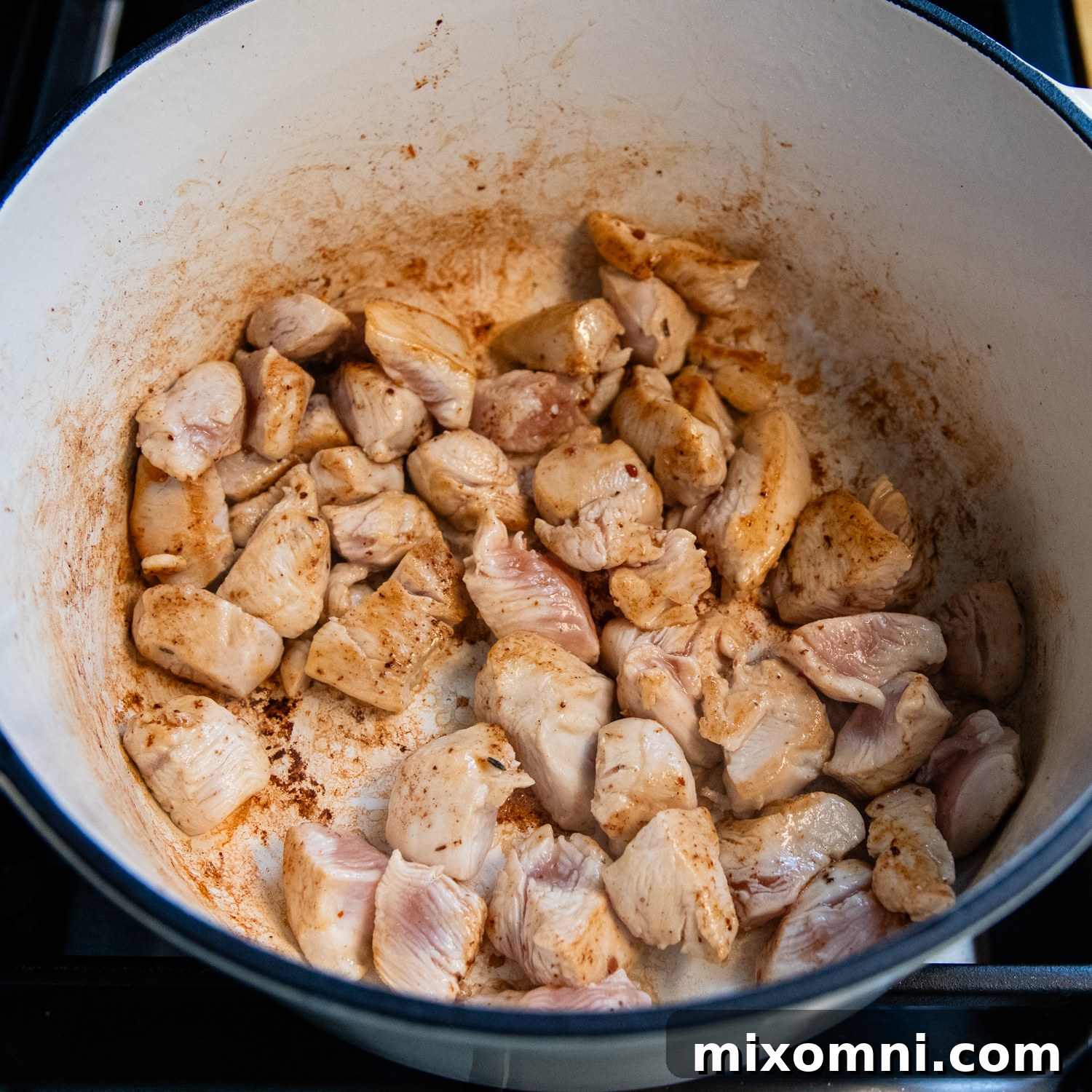 Chicken pieces searing in a hot pot after sausage has been removed.