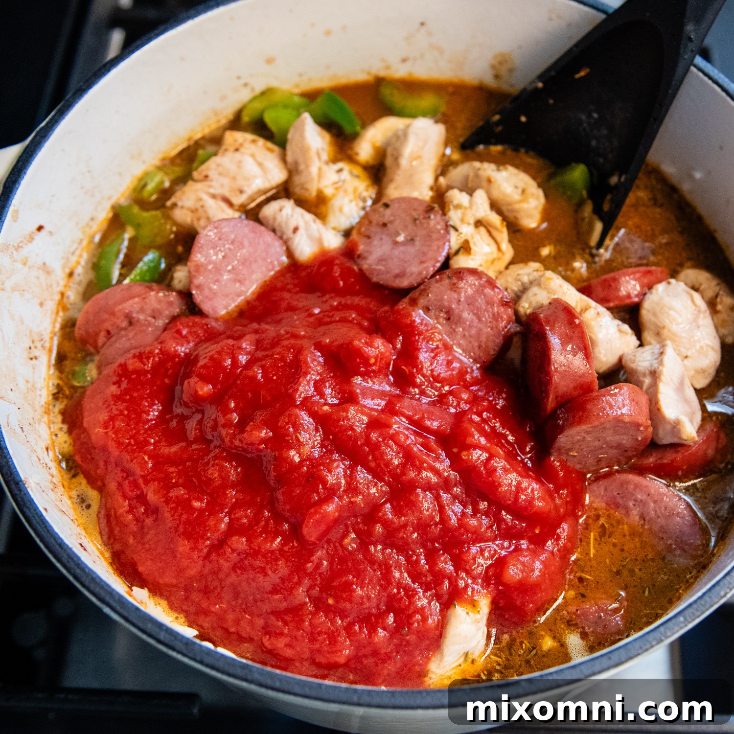 Chicken broth, crushed tomatoes, and tomato paste added to the jambalaya mixture.