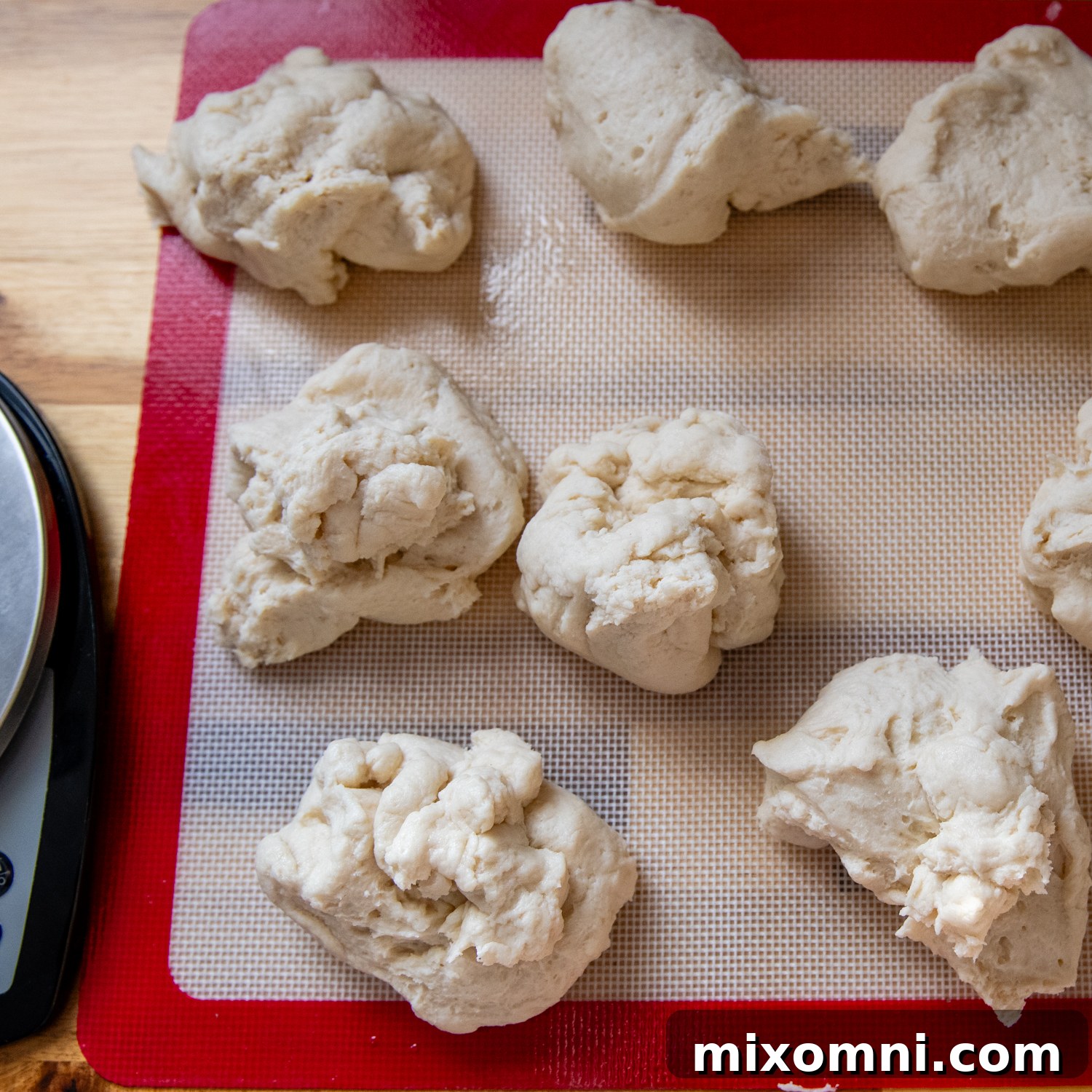 Evenly divided balls of gluten-free English muffin dough resting on a baking mat.