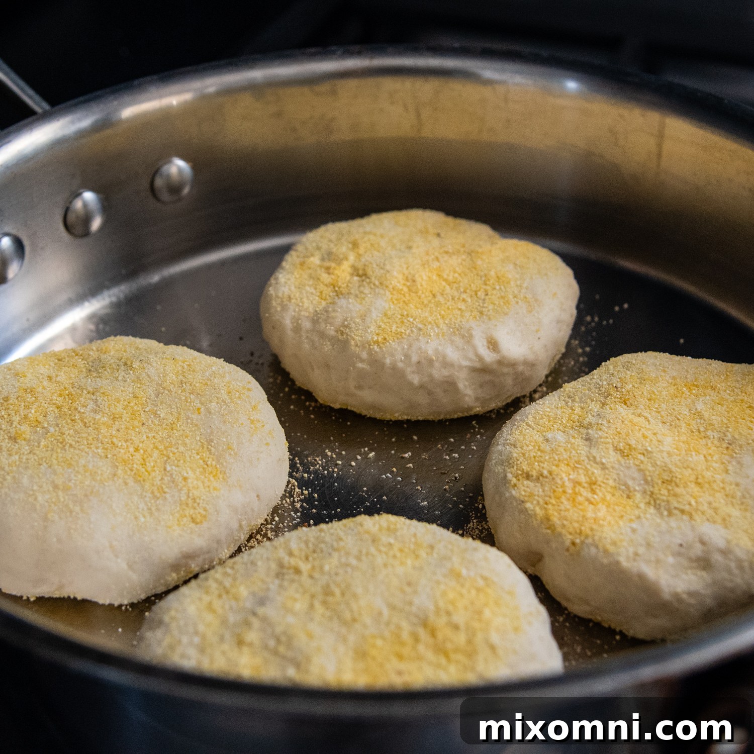 Gluten-free English muffins frying in a skillet to achieve a golden crust.