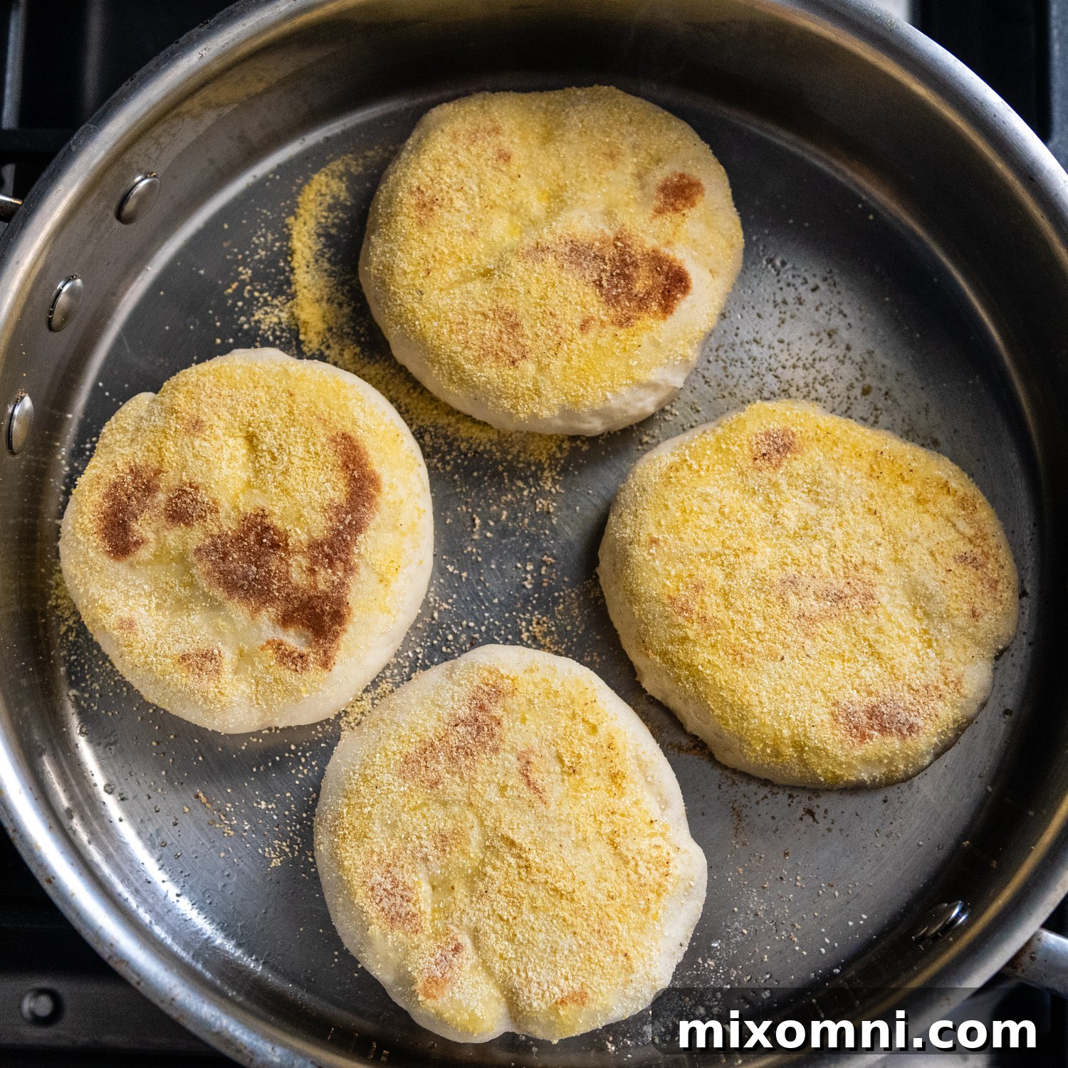 Overhead shot of perfectly browned gluten-free English muffins frying in a pan, ready for the oven.