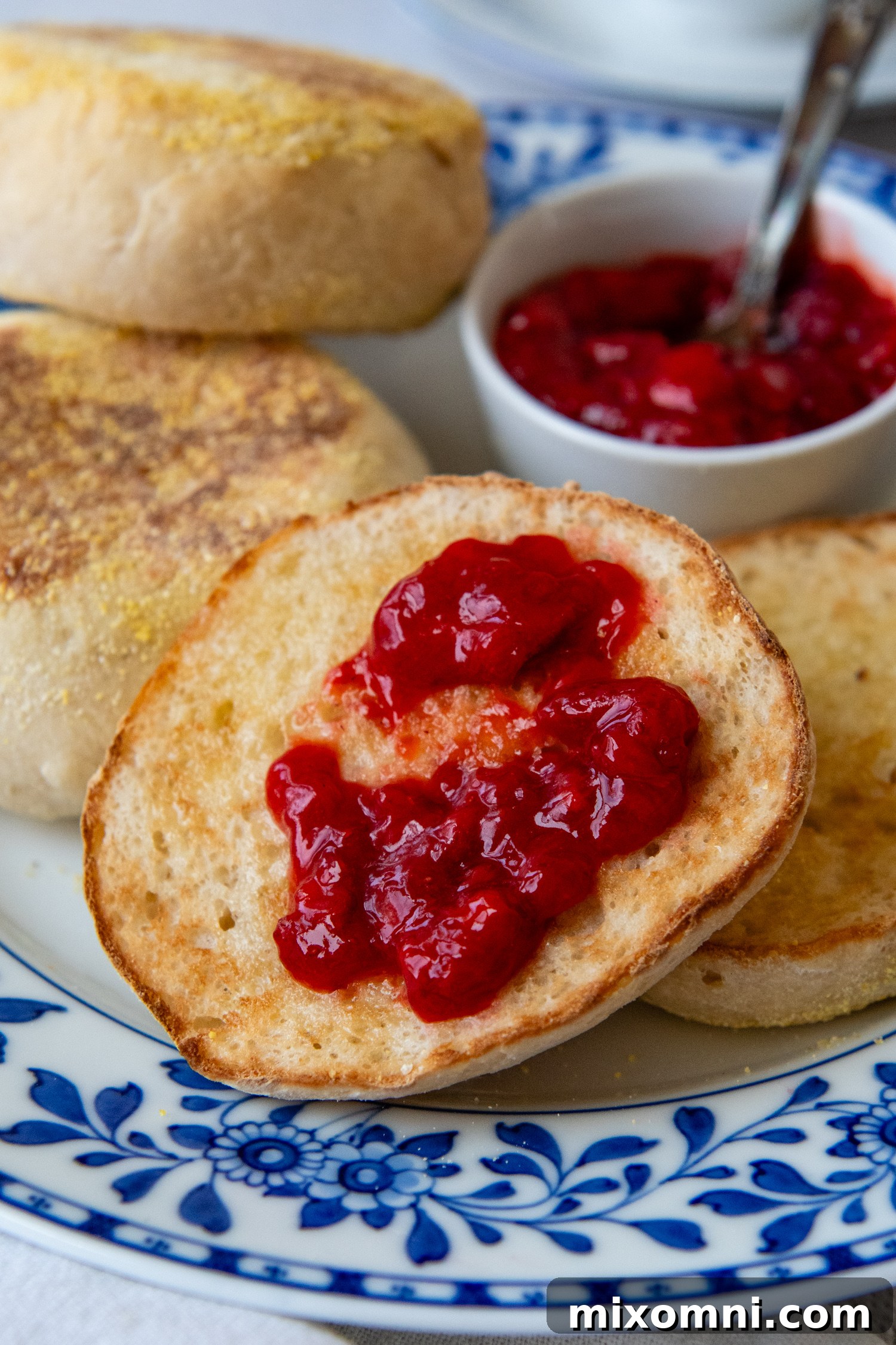 Close-up of a perfectly sliced open gluten-free English muffin, revealing its airy interior and topped with vibrant preserves.
