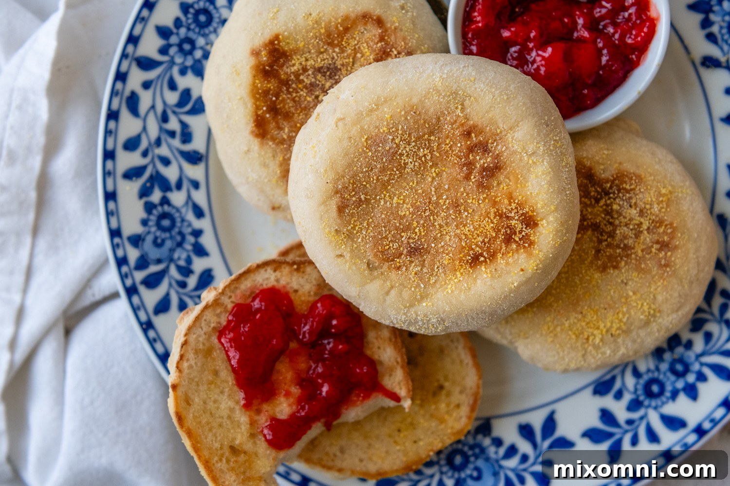 Multiple golden-brown gluten-free English muffins arranged on a plate, with one showcasing its toasted, textured exterior.