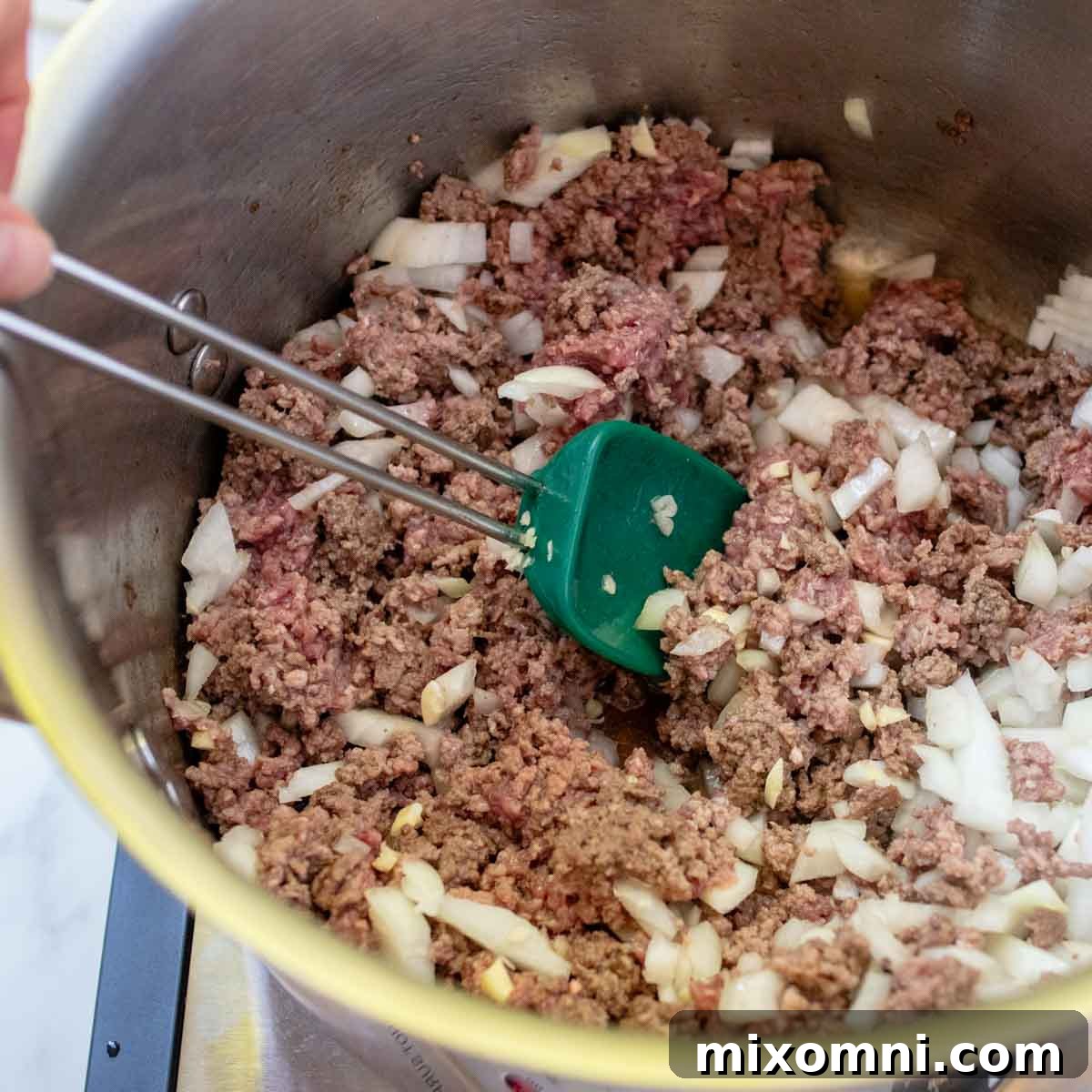 A large pot on the stove, showing ground beef, onions, and minced garlic browning together, creating a fragrant base for the soup.