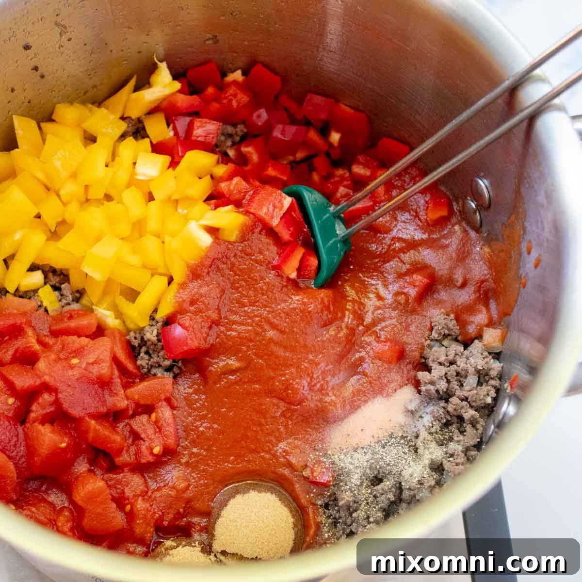 Various vibrant ingredients including diced tomatoes, bell peppers (red and yellow), and seasonings being added to the browned beef mixture in the soup pot.