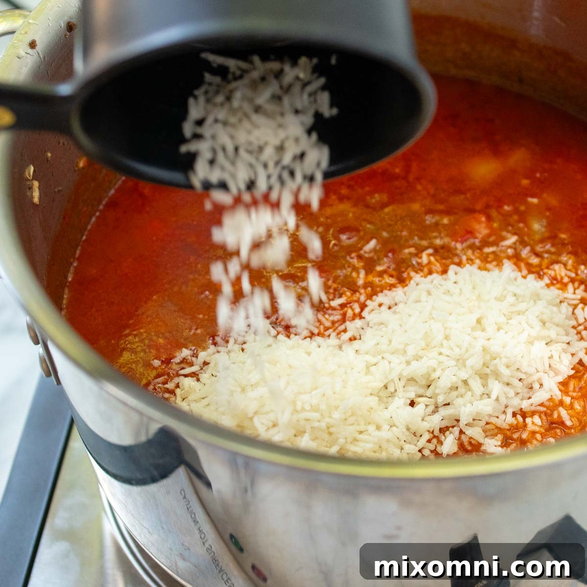 Instant rice being stirred into the simmering stuffed pepper soup, absorbing the rich tomato broth.