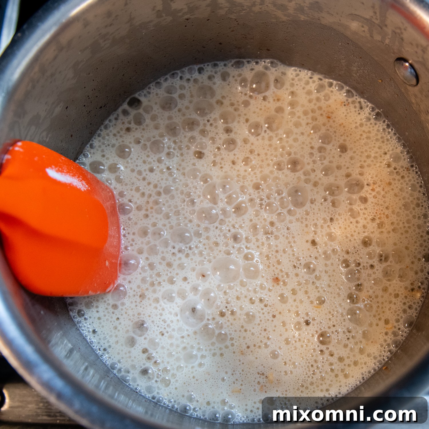 A saucepan filled with a creamy, white sauce, gently simmering on a stovetop, capturing its rich texture and warmth.