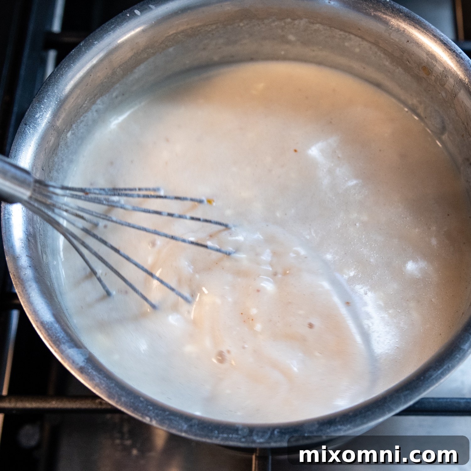 A close-up of a whisk blending a rich, golden cheese sauce in a saucepan, creating a smooth and creamy consistency.