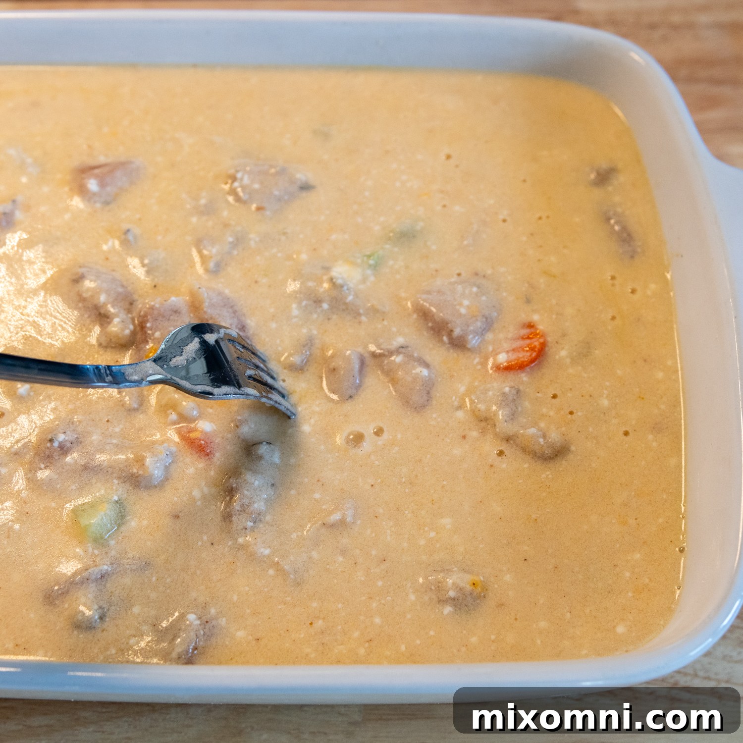 A fork gently mixing the ingredients within a baking dish, ensuring the creamy sauce, rice, chicken, and vegetables are evenly combined.