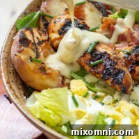 honey mustard dressing being poured over grilled chicken salad