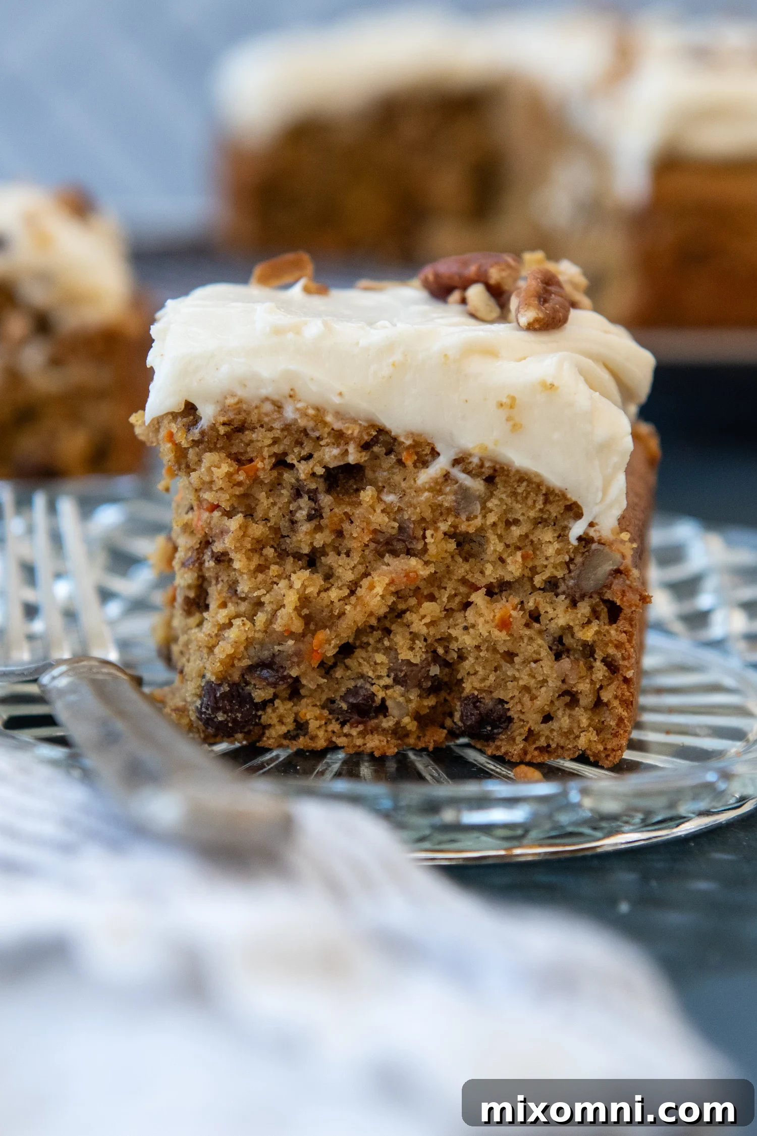 A perfectly sliced piece of moist gluten-free carrot cake with luscious browned butter cream cheese frosting, sitting on an elegant glass plate.