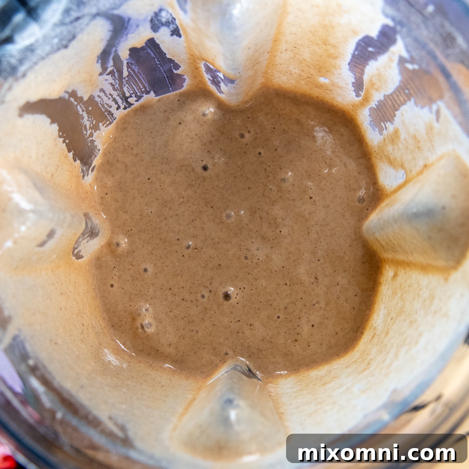 Various carrot cake ingredients, including spices, sugars, and wet components, being blended with oat flour in a blender to form a smooth batter.