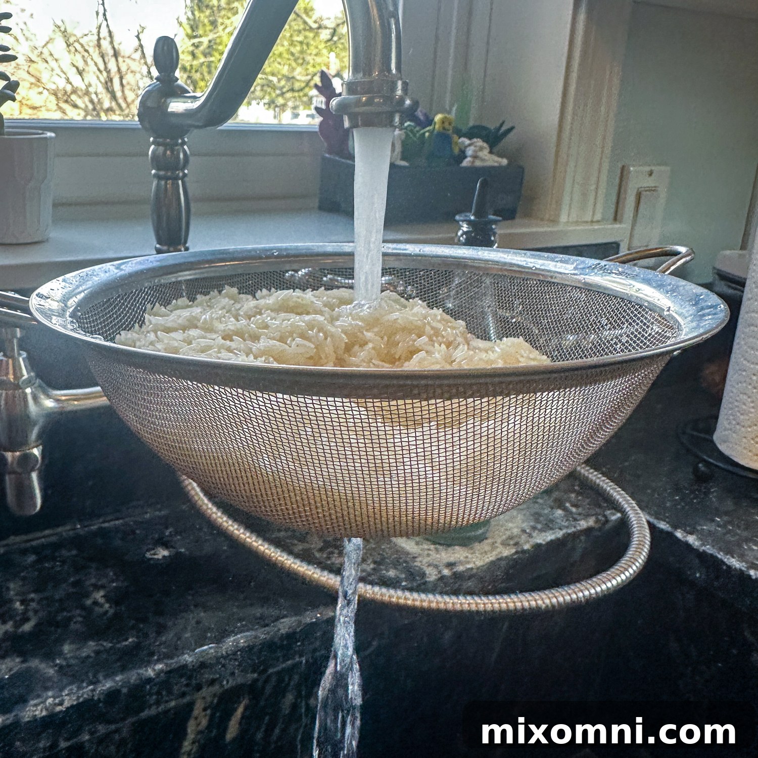Raw jasmine rice being rinsed thoroughly in a colander under running water, demonstrating the essential first step for non-mushy fried rice.