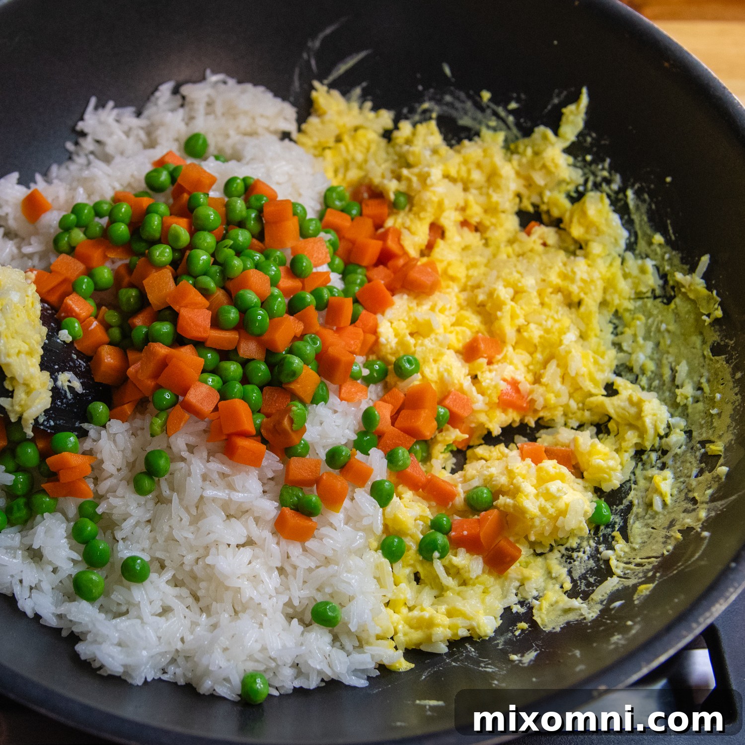Gluten-free fried rice in a black wok, seasoned with green onions, peas, carrots, and soy sauce, nearing completion.
