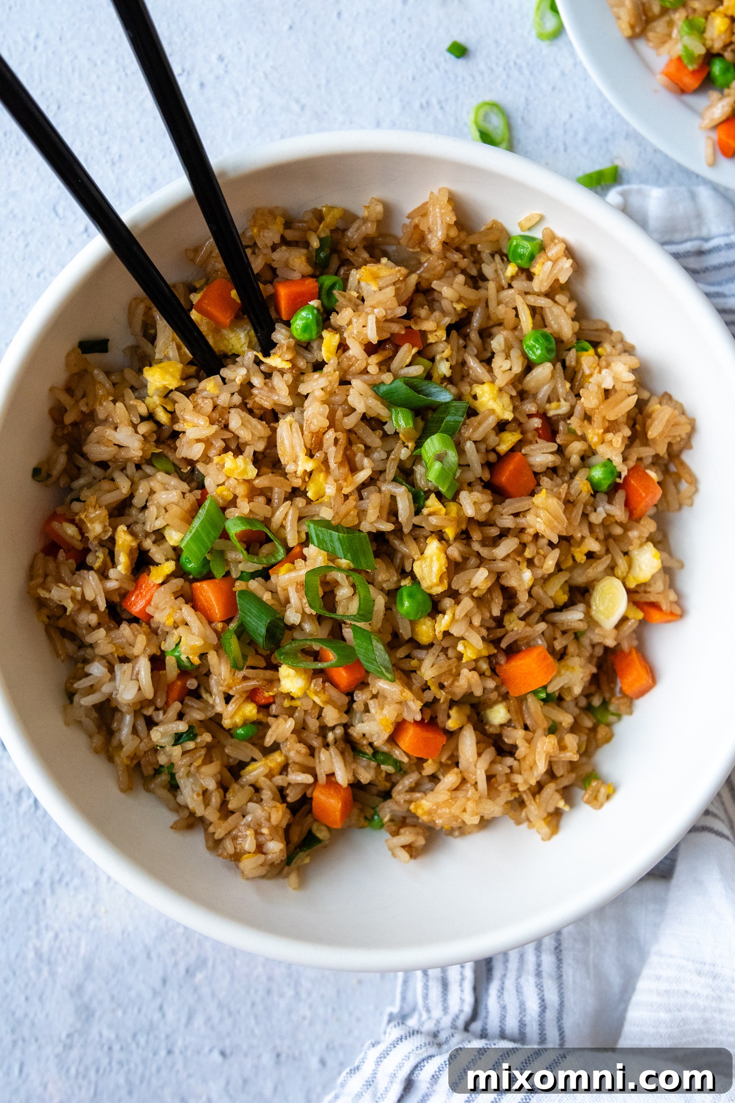 Close-up overhead shot of gluten-free fried rice garnished with fresh green onions in a white bowl, with chopsticks poised to pick up a mouthful.