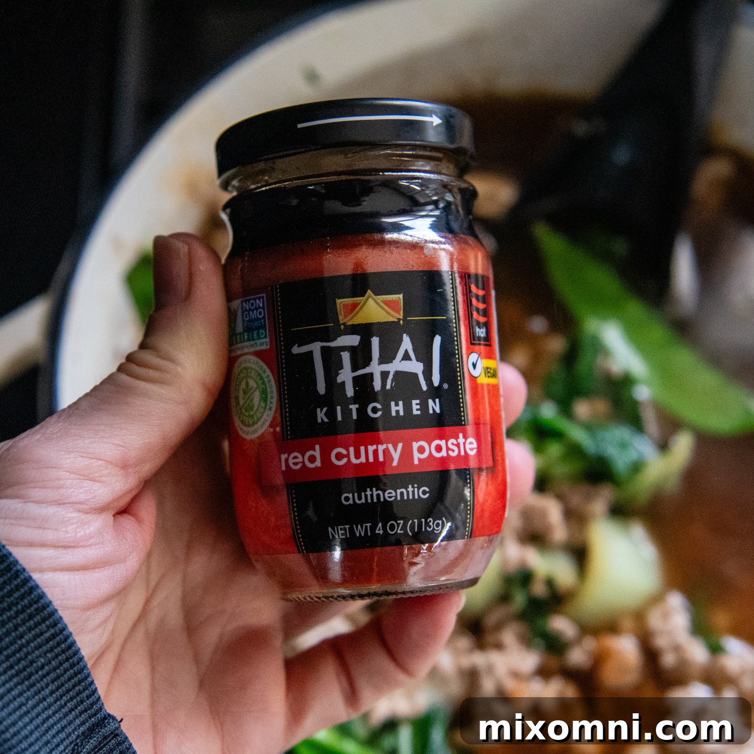 Hand holding a jar of red curry sauce.