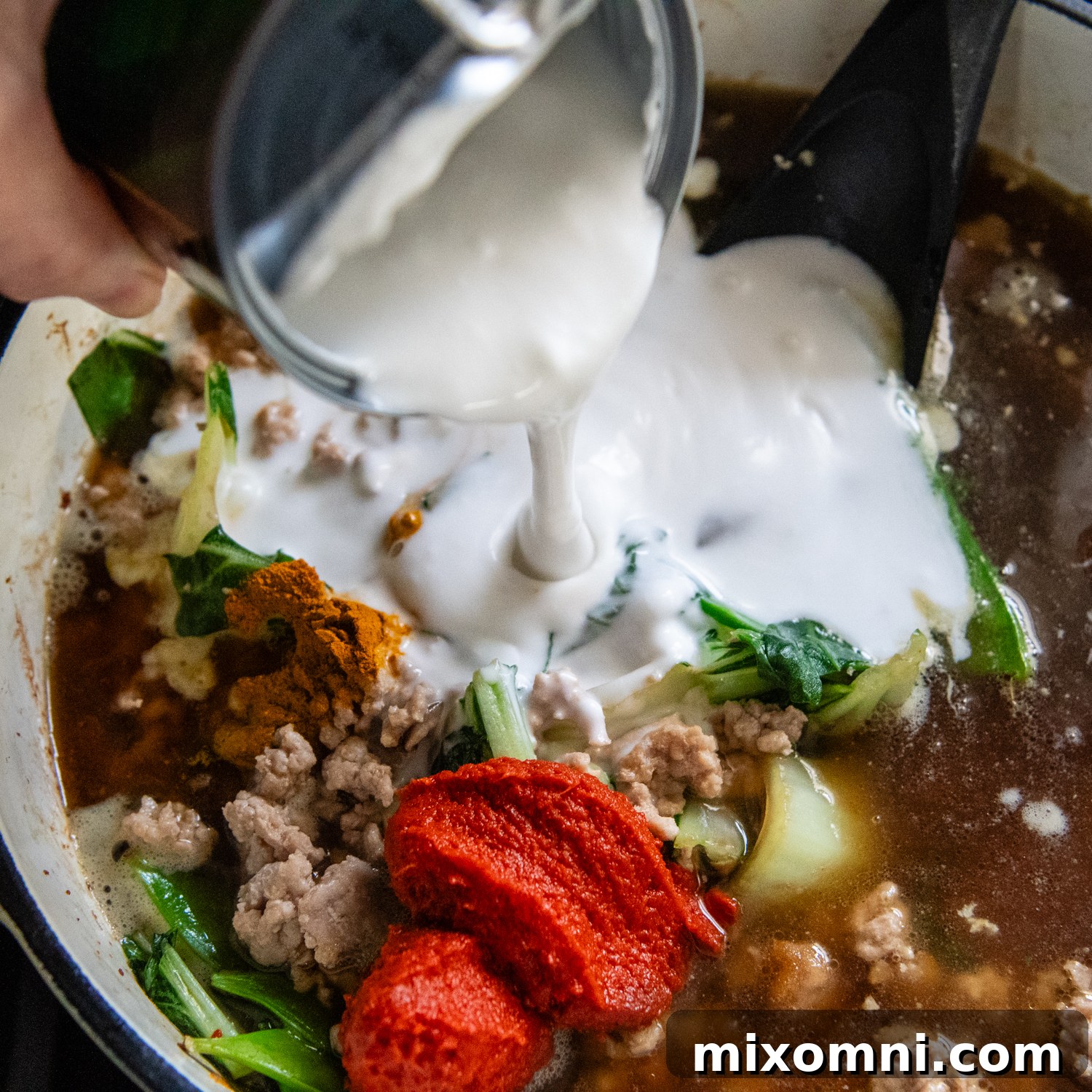 Coconut milk being poured into ramen.