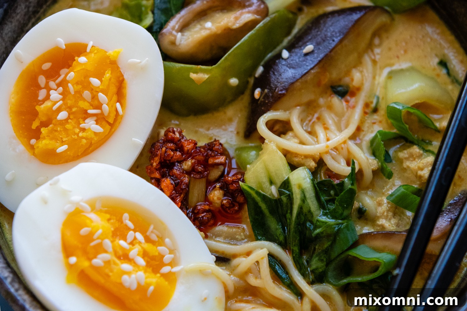 Close up of ramen that includes whole eggs, chili seasonings, and greens.