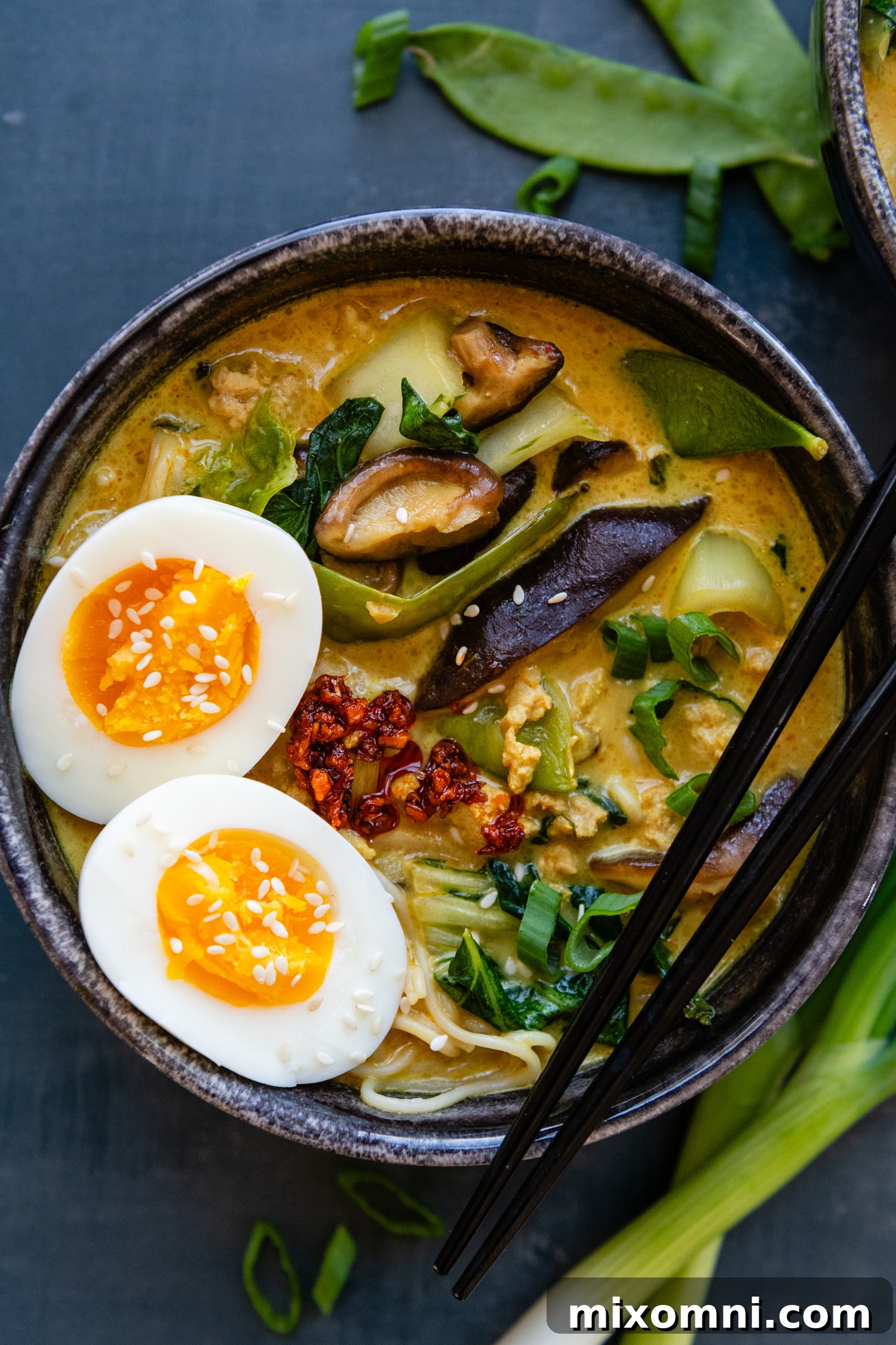 Bowl of ramen with whole eggs and seasonings with chopsticks.